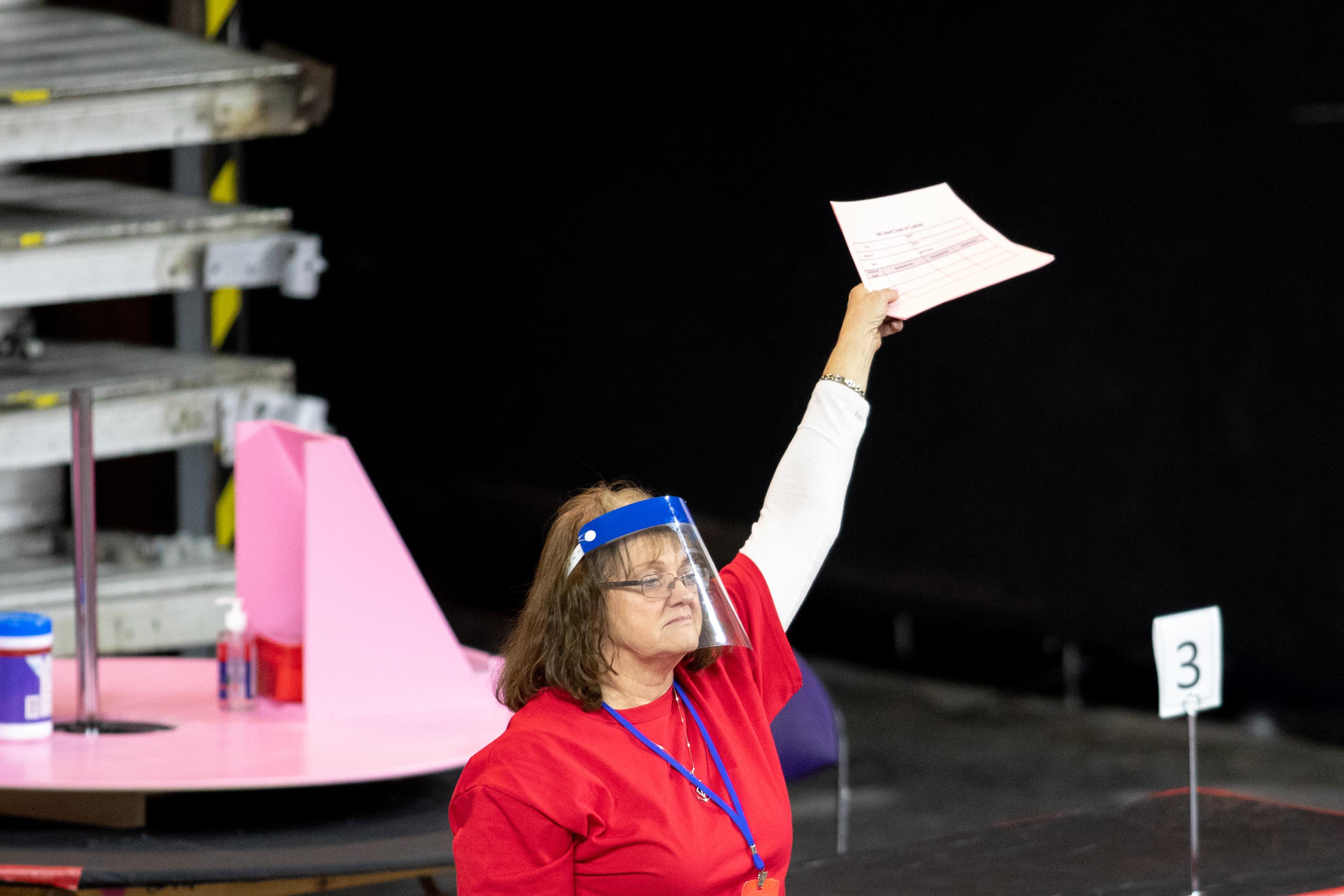 A woman wearing a visor holds up a piece of paper in the recount facility.