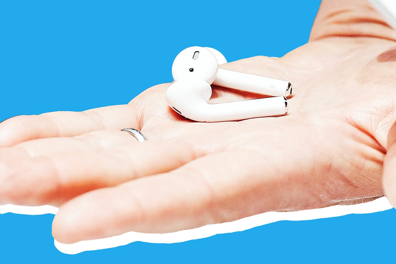 A hand with a wedding band holds a pair of AirPods.
