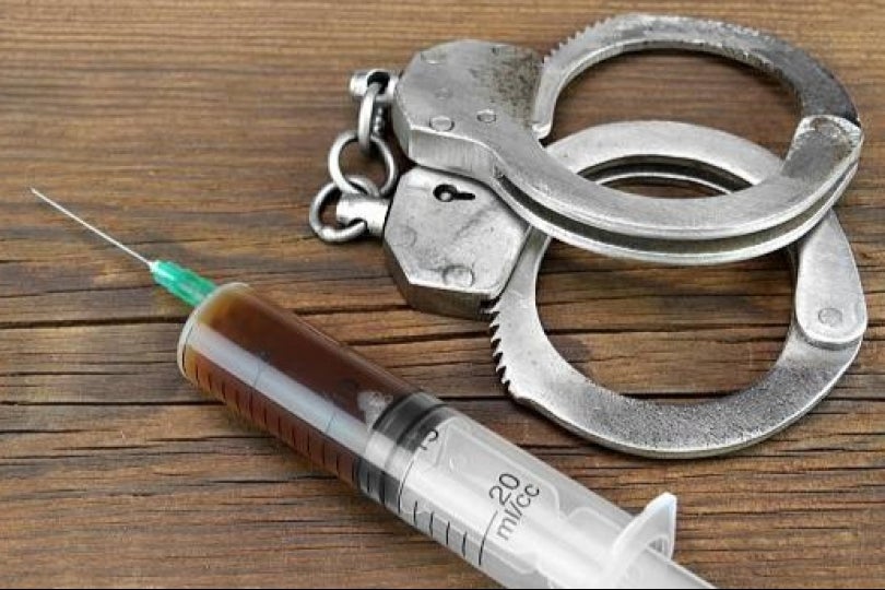 A needle featuring lethal injection drugs next to a pair of handcuffs on a wooden table or countertop