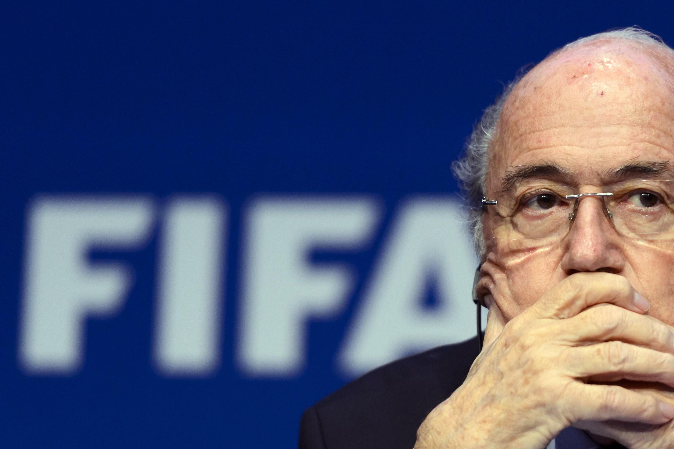 Fifa President Sepp Blatter eyes someone asking a question at the press conference with both of his hands placed over his mouth.