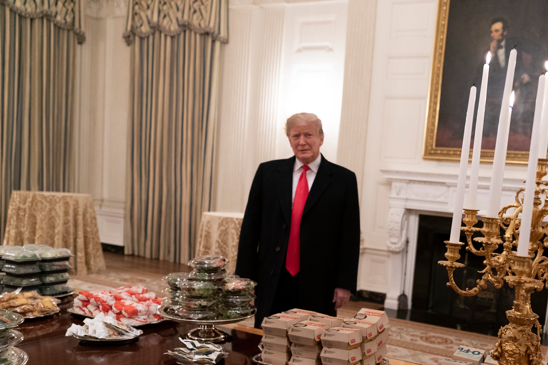 Trump stands in front of a table covered in fast food with a portrait of Abraham Lincoln behind him.