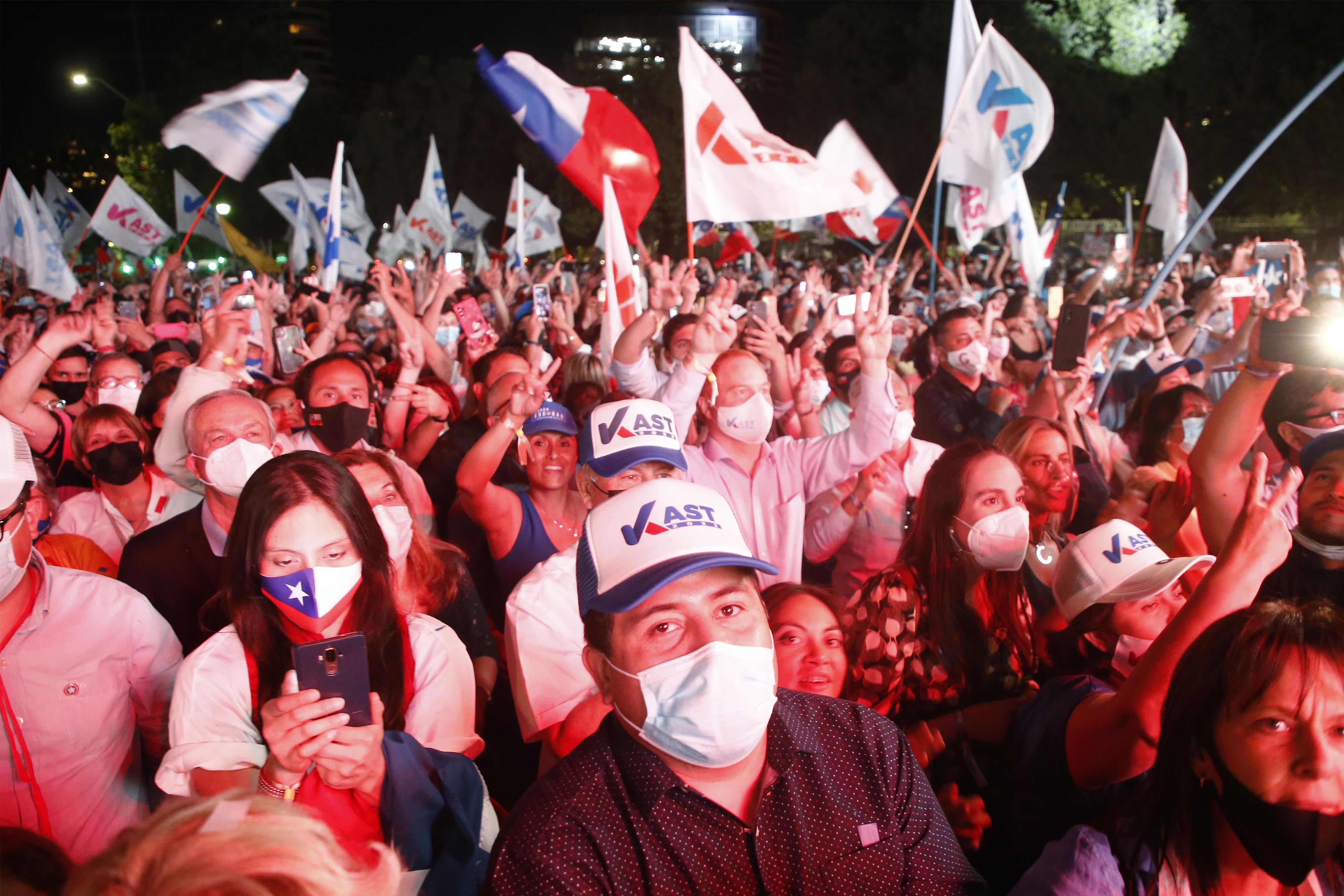 Campaign supporters standing in a crowd waving flags and signs.