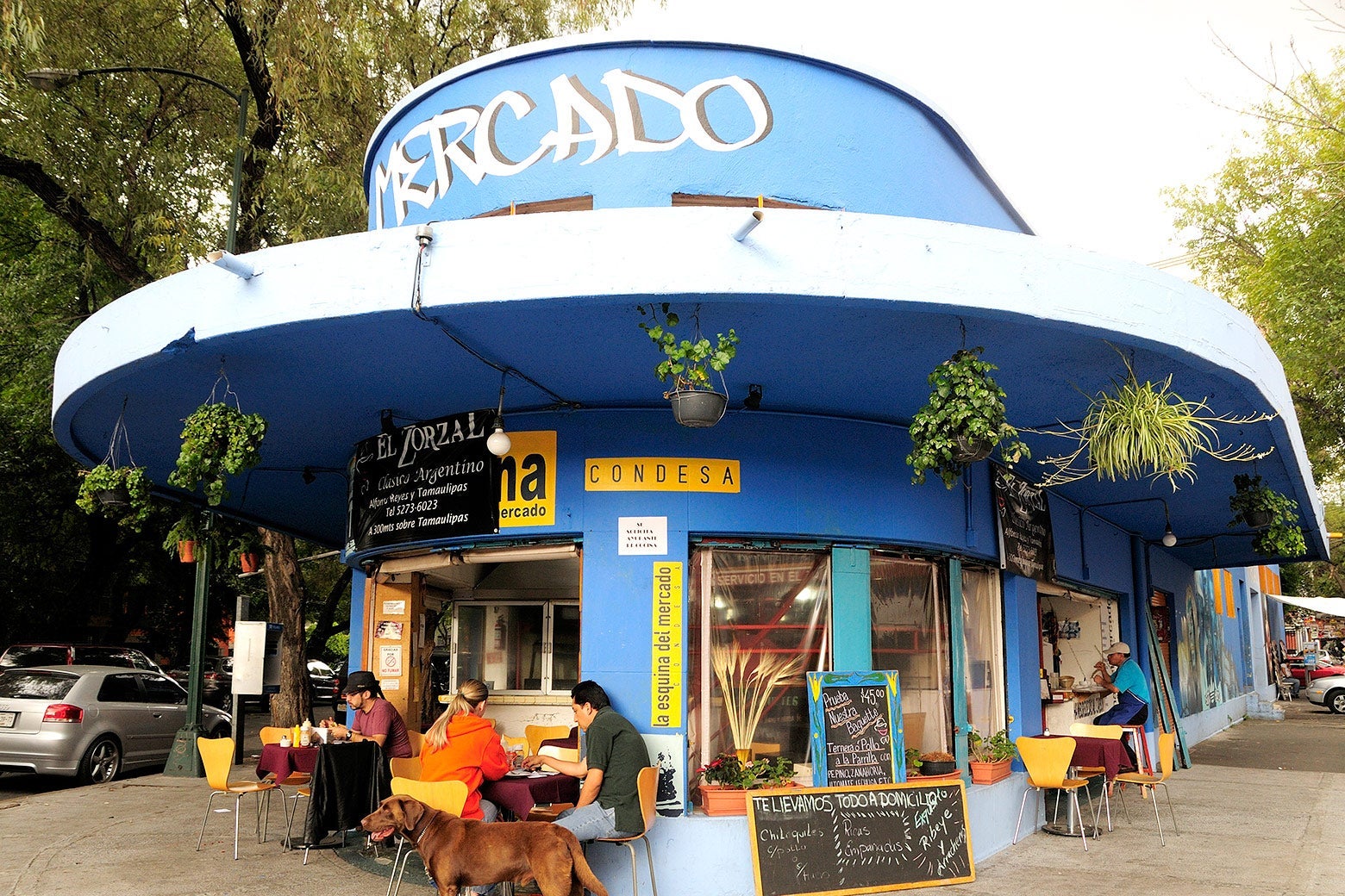 Customers sit at outdoor tables outside a blue restaurant.