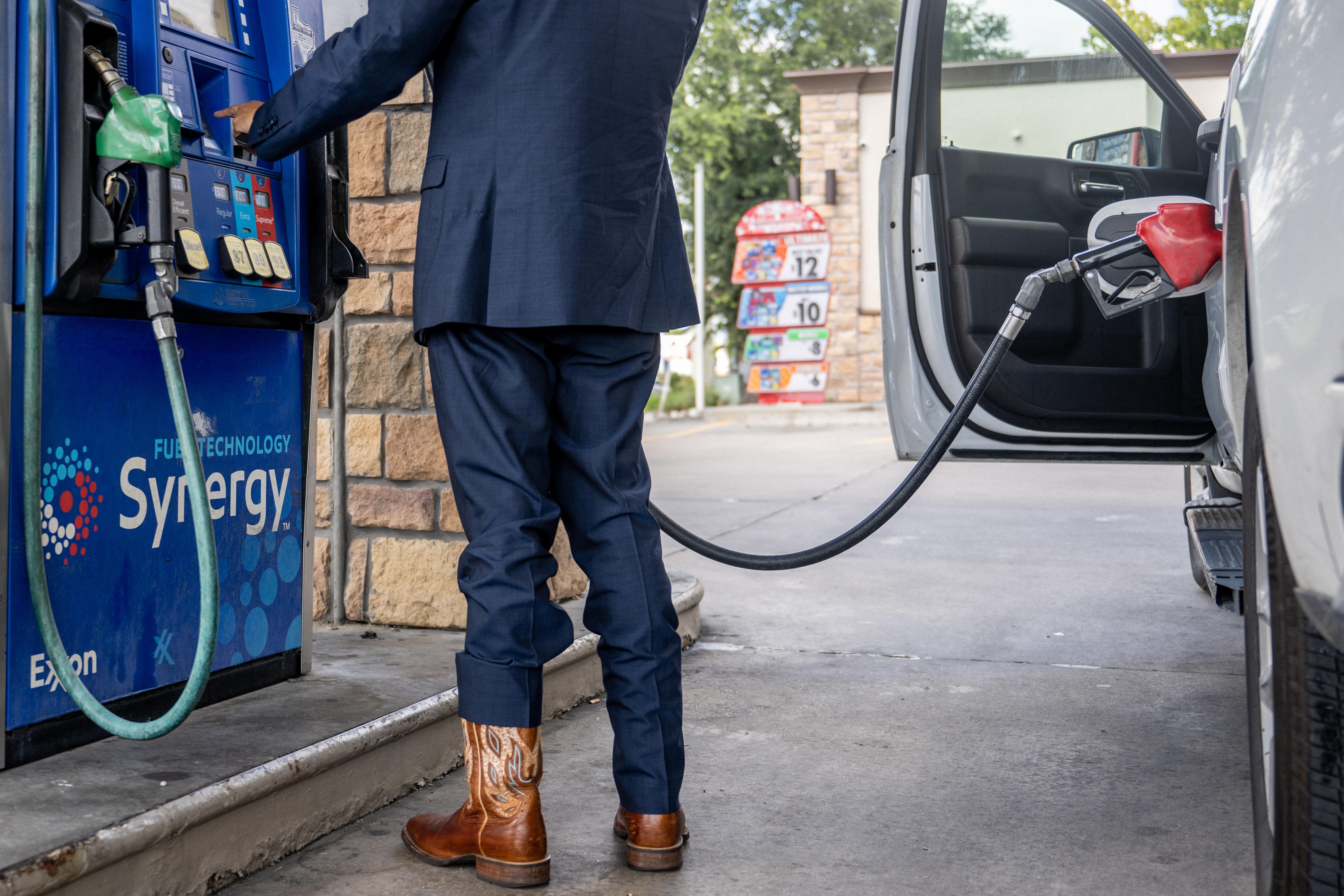 A boots-wearing man pumping gas into his car.