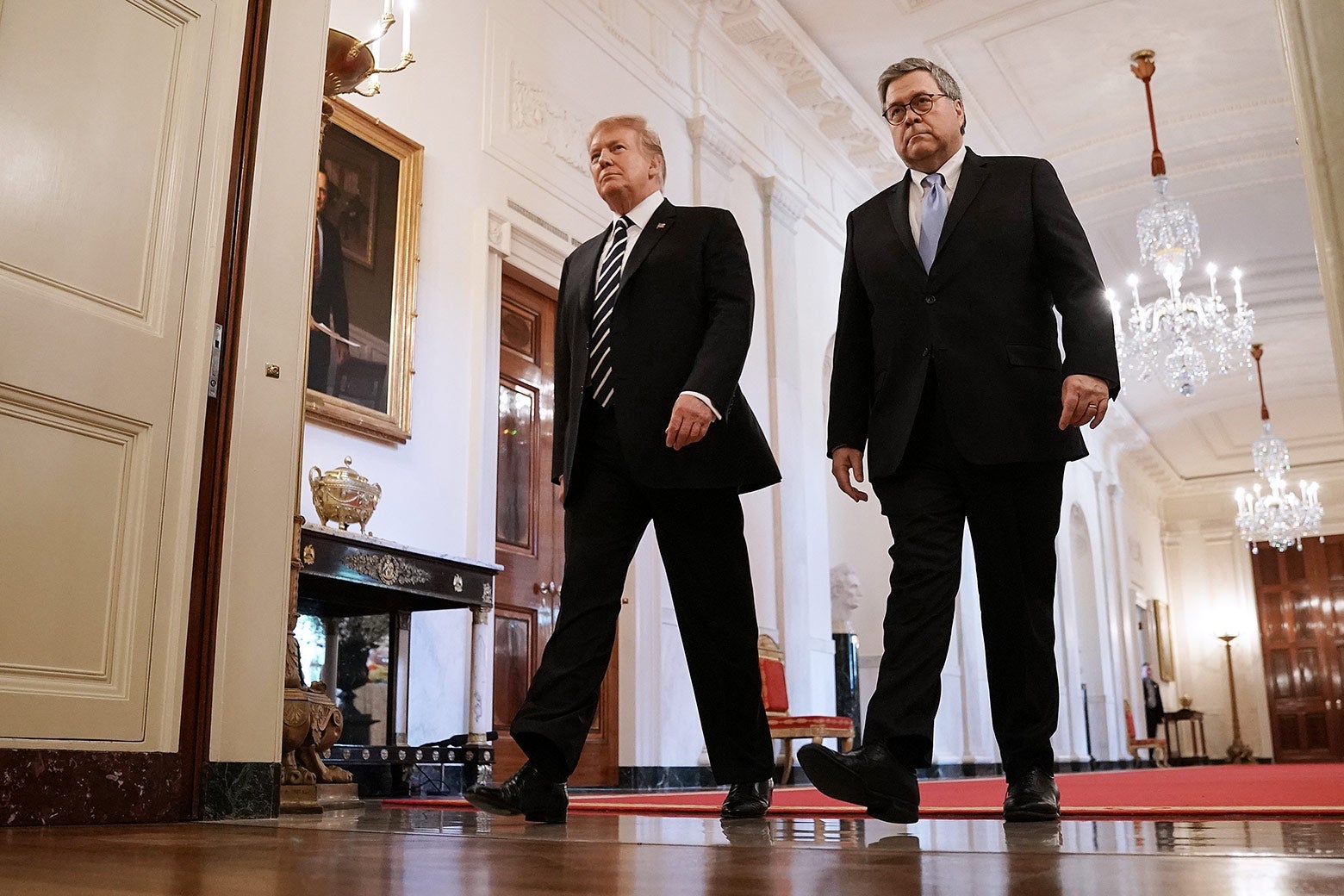 Donald Trump and William Barr walk down a hallway with chandeliers.