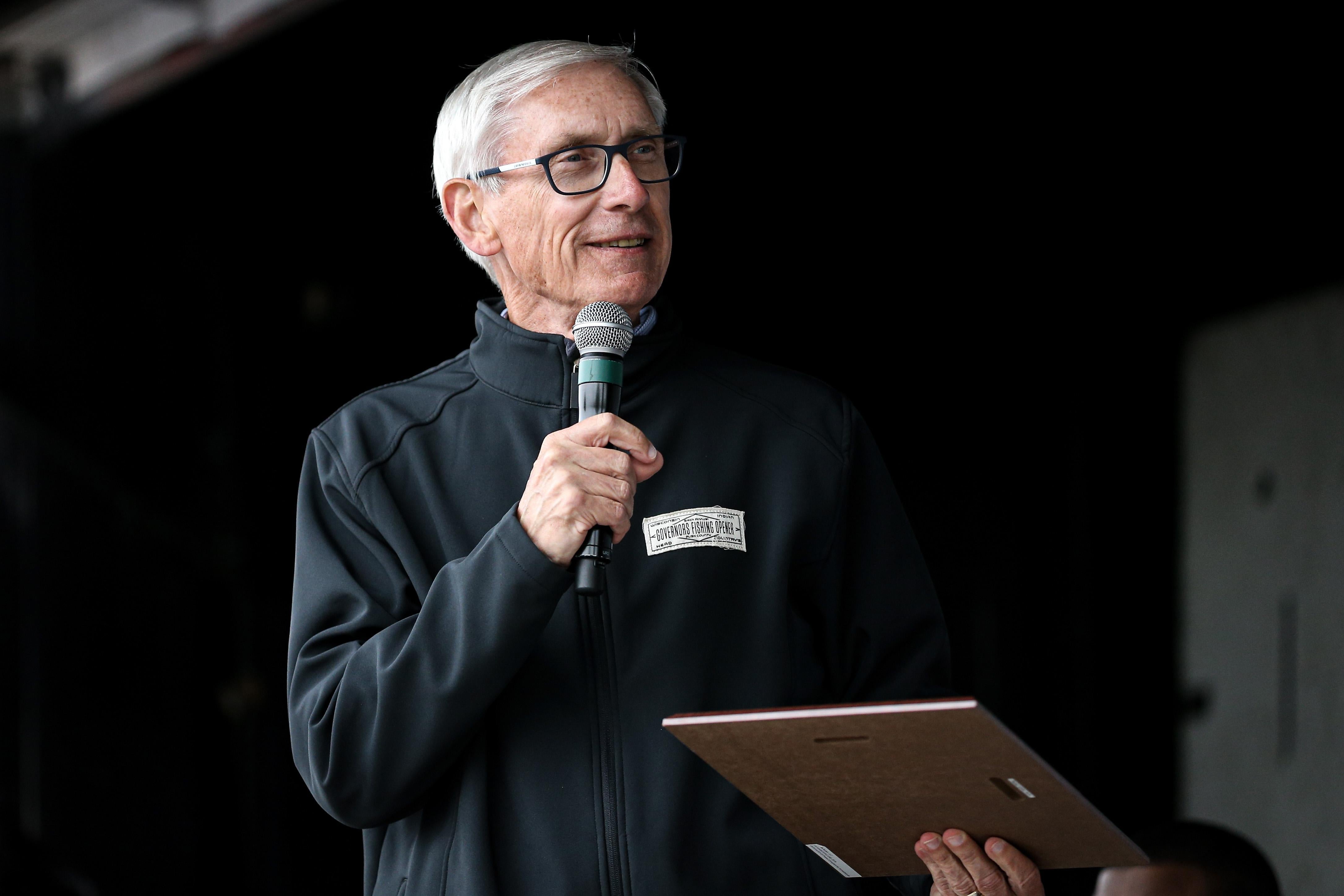 Evers speaks to the crowd, holding a mic in one hand and a clipboard in the other