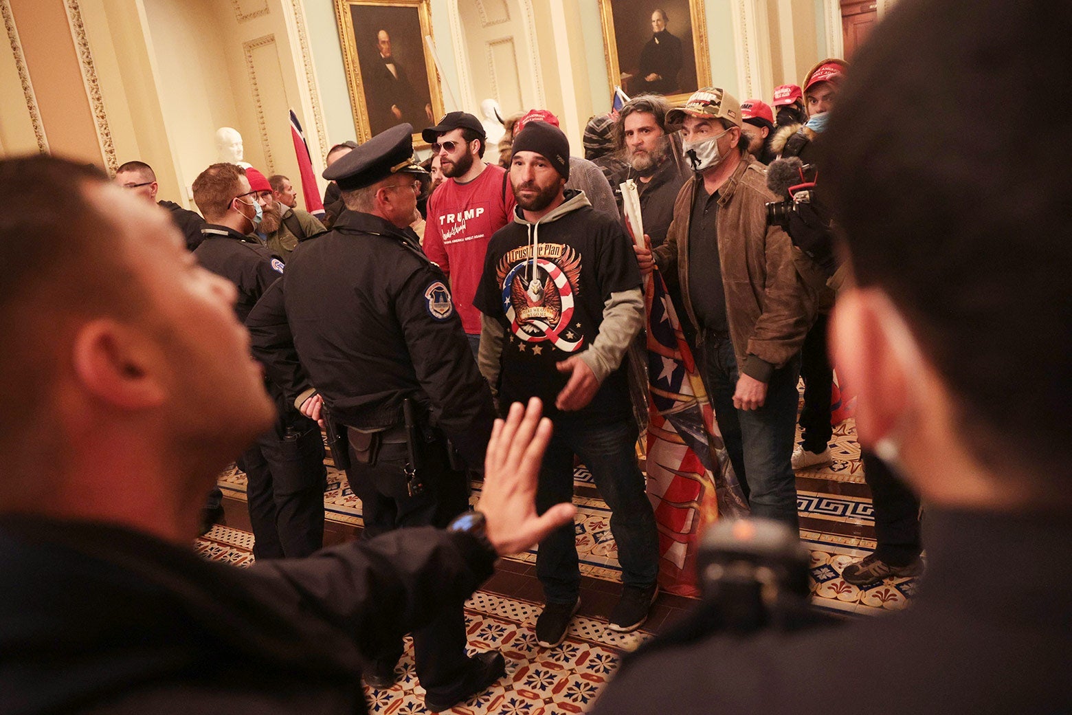 Multiple maskless and masked Trump supporters gather inside the Capitol Building. Capitol Police officers engage with them.