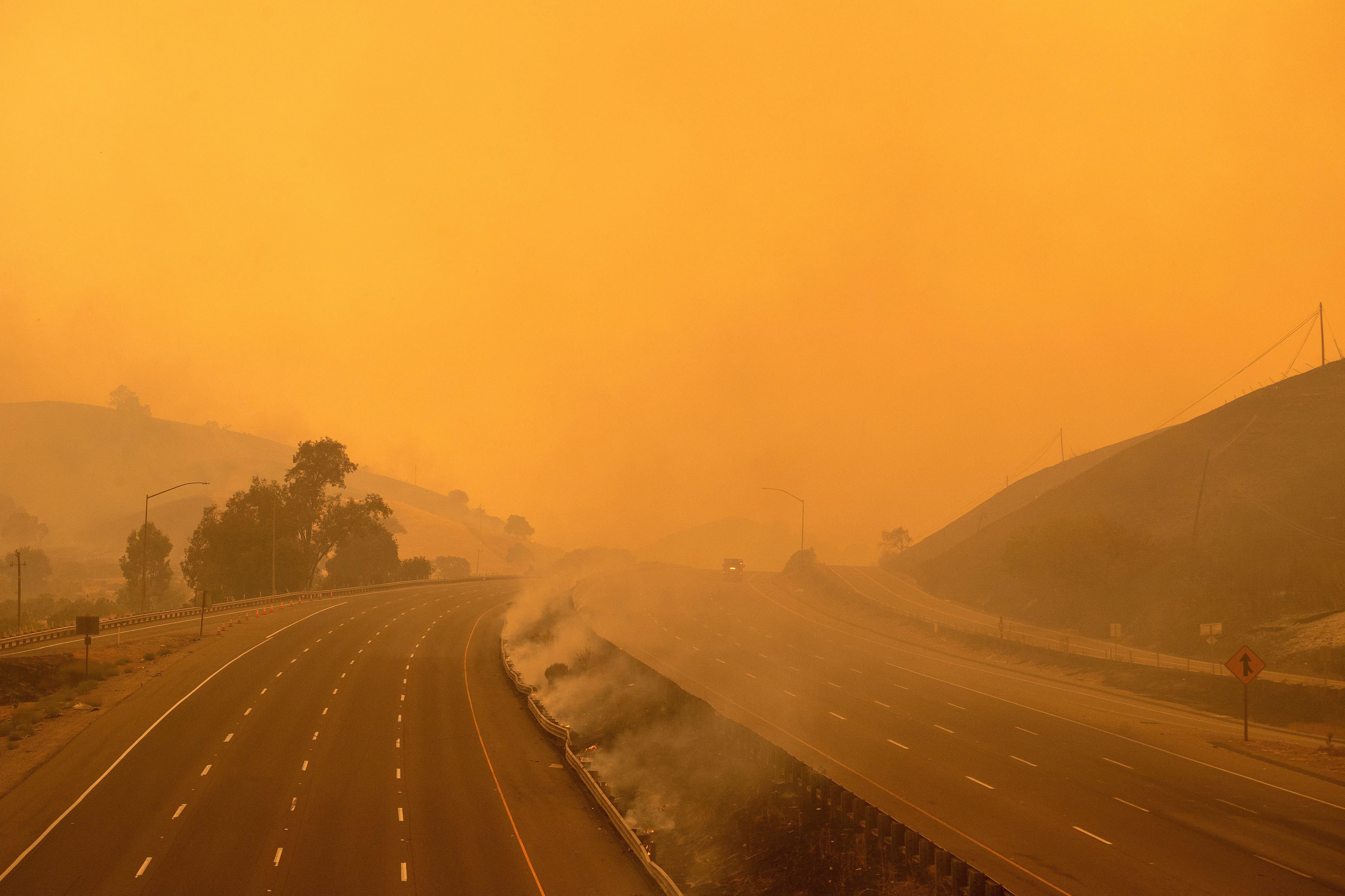 A firetruck drives along a highway amid wildfire smoke.