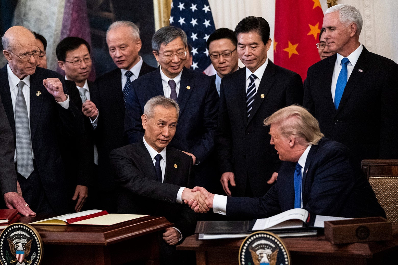 Trump shakes He’s hand while stakeholders stand around them.