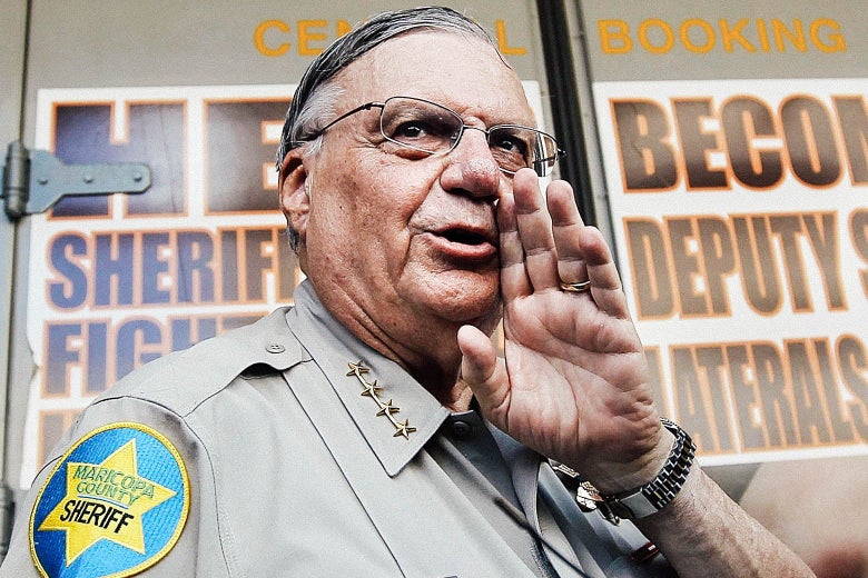 Arpaio in uniform standing in front of the central booking doors with his hand on the side of his mouth as if calling out