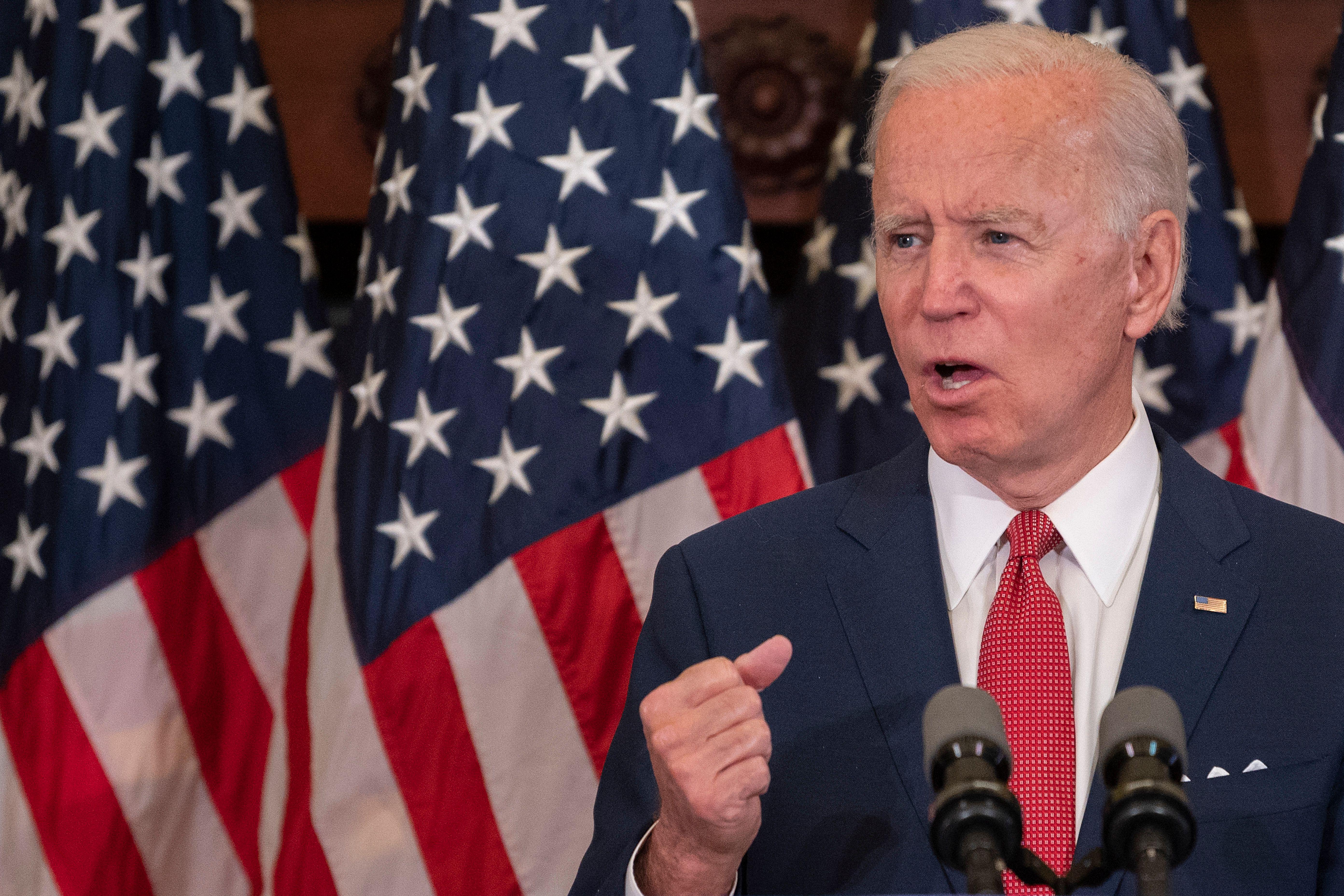 Biden speaks at a mic in front of American flags