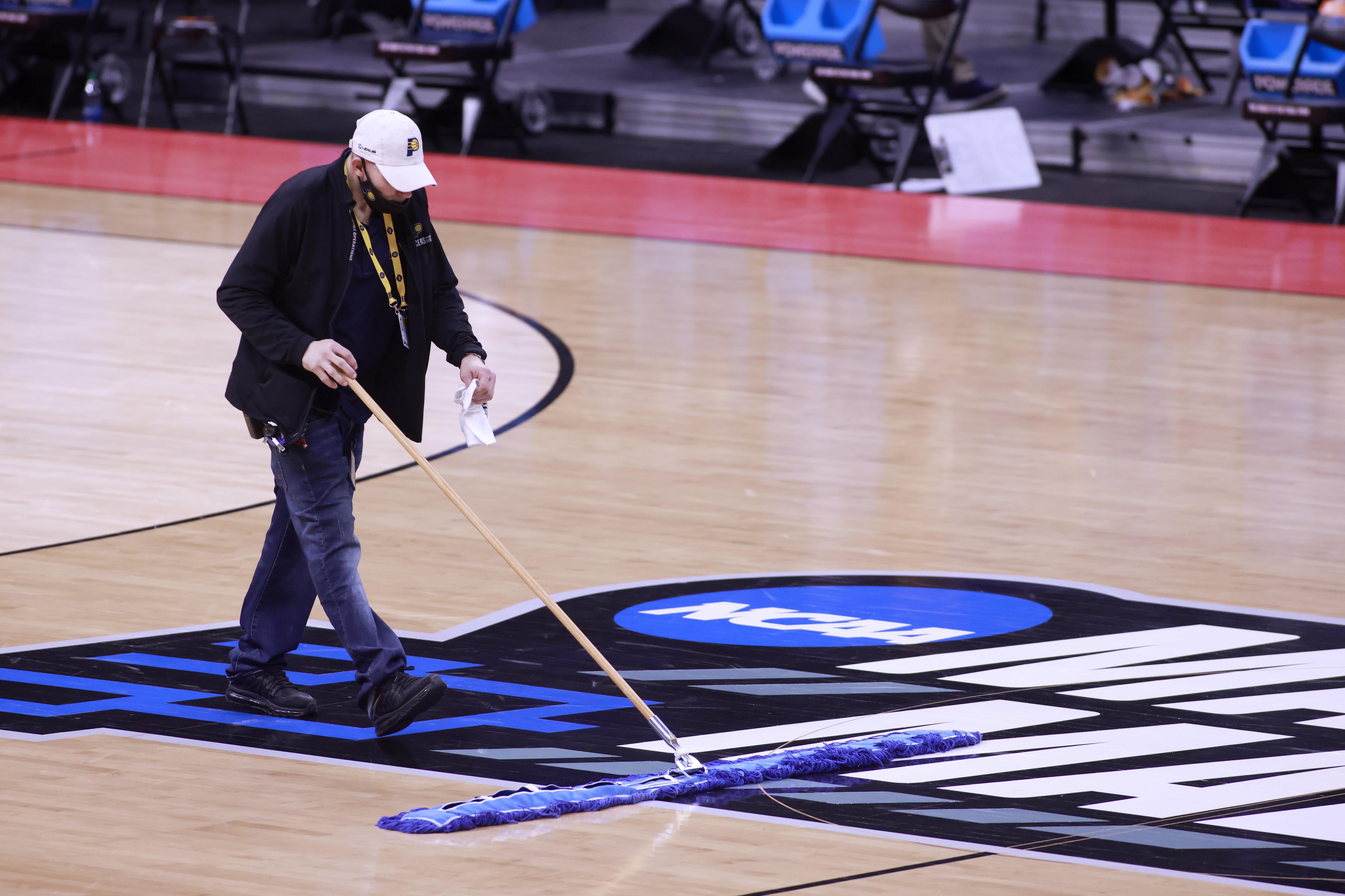 A man sweeps the basketball court with the March Madness logo on it, in Indianapolis