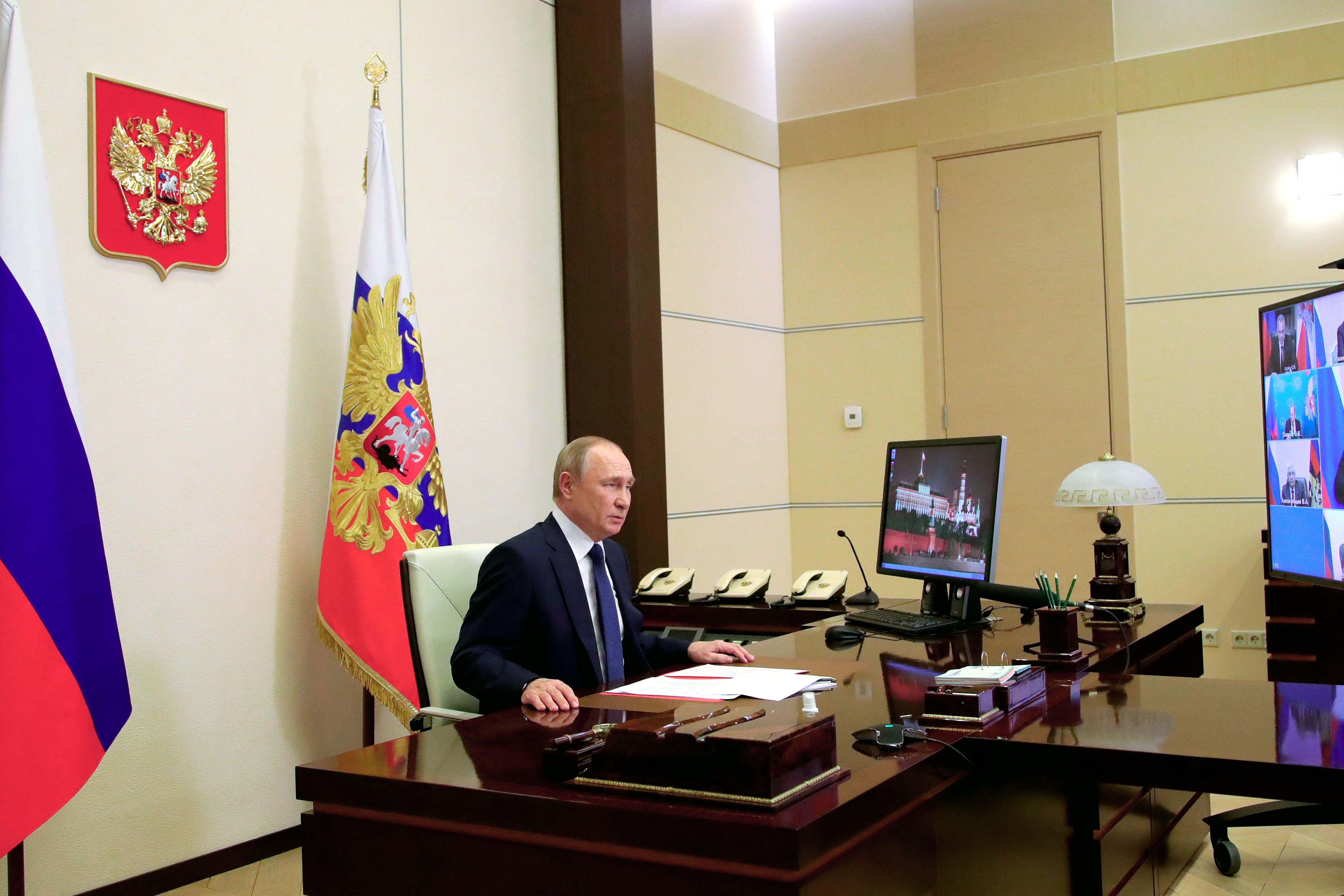 Putin sitting in front of a TV with a bunch of different faces.