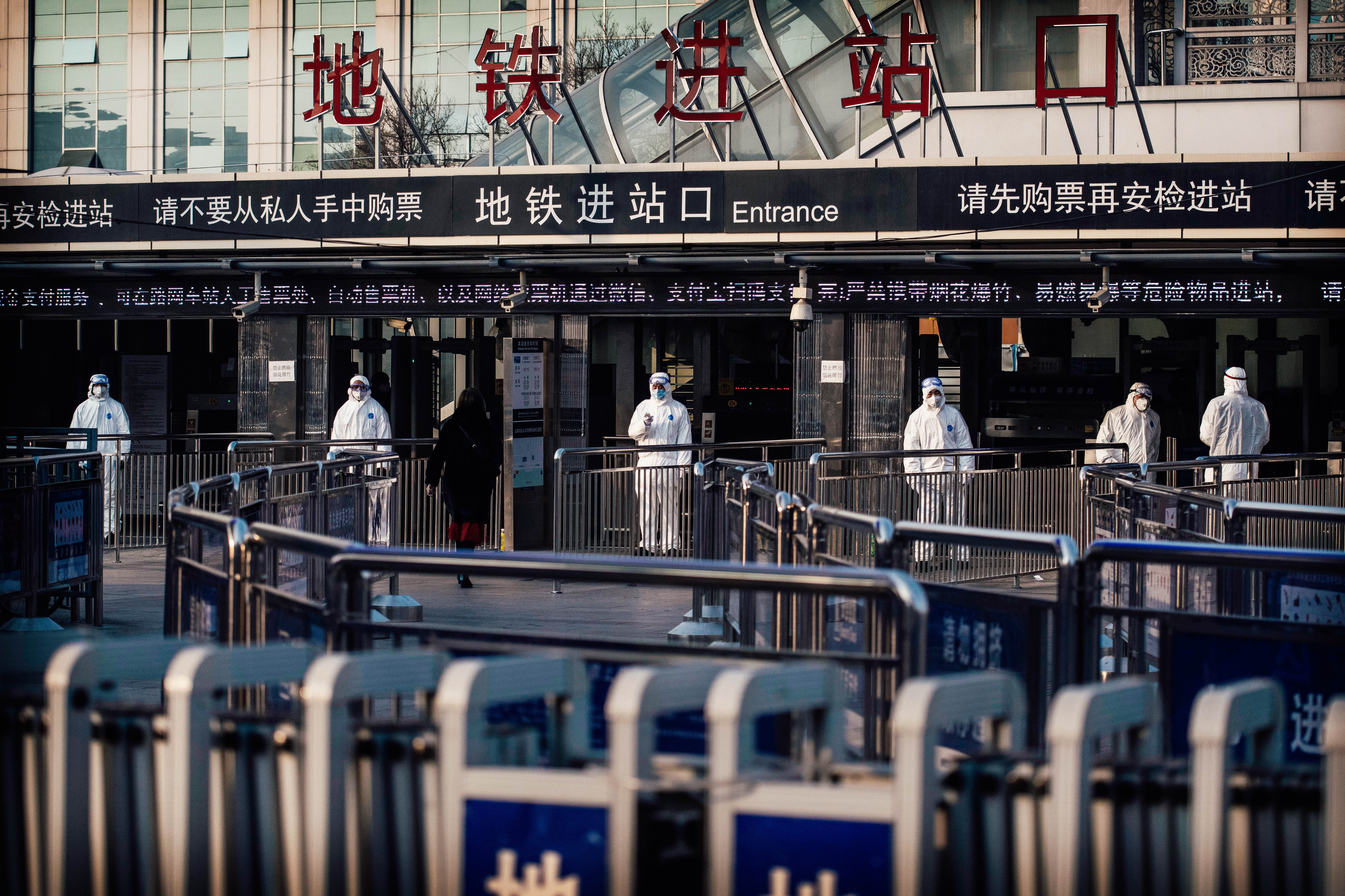 Workers in protective suits stand in a train station.