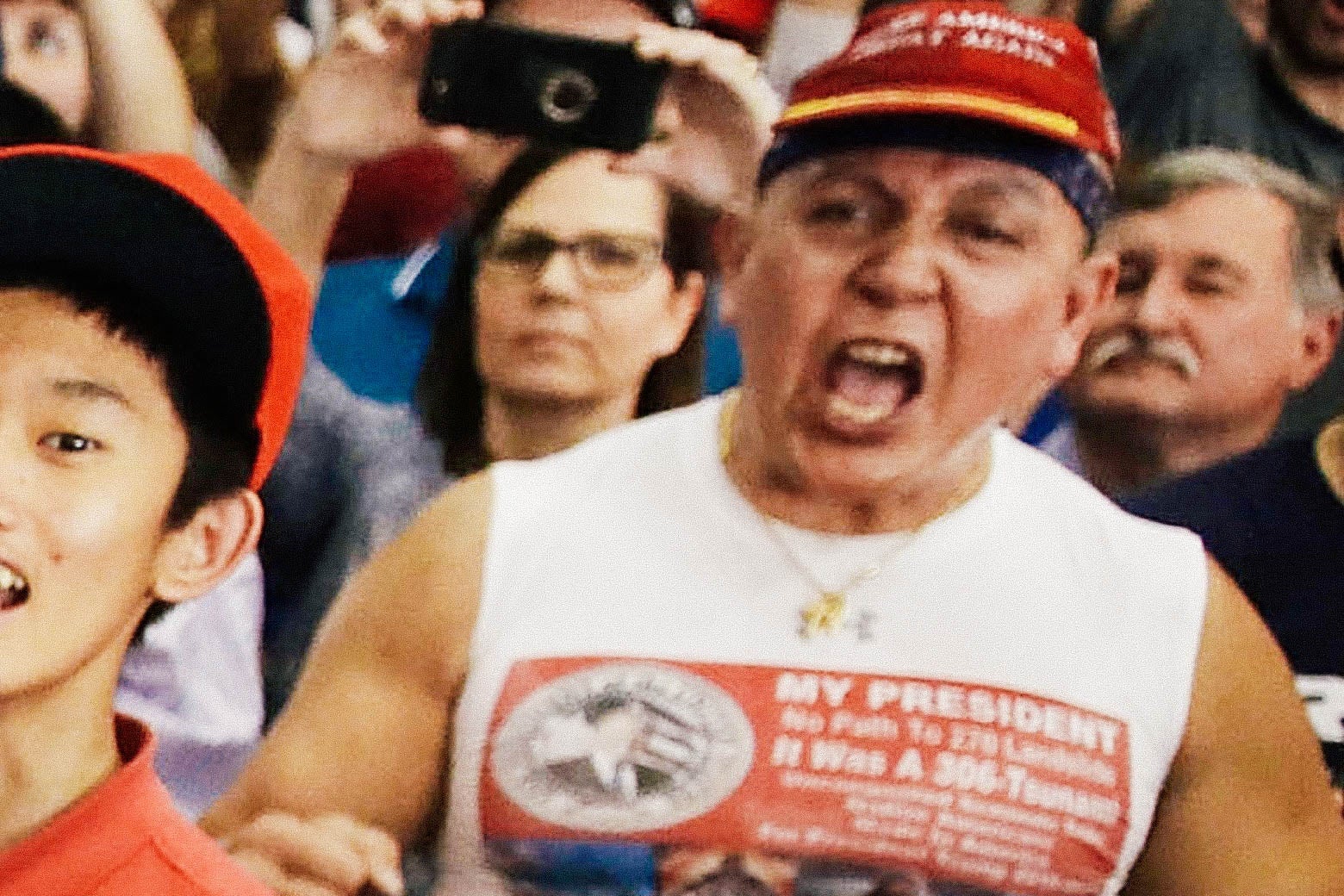 Sayoc wearing a MAGA hat and pro-Trump shirt and yelling in a crowd of other Trump supporters.