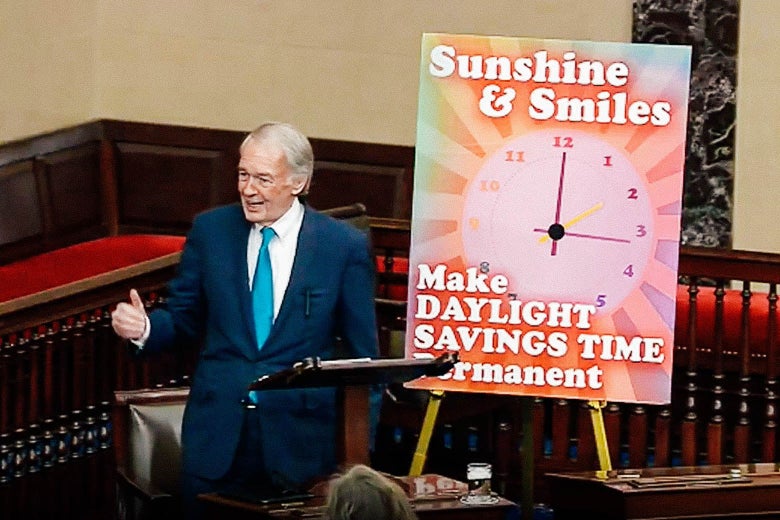 Markey speaks on the Senate floor next to a poster of a clock that says "Sunshine and Smiles: Make Daylight Savings Time Permanent"