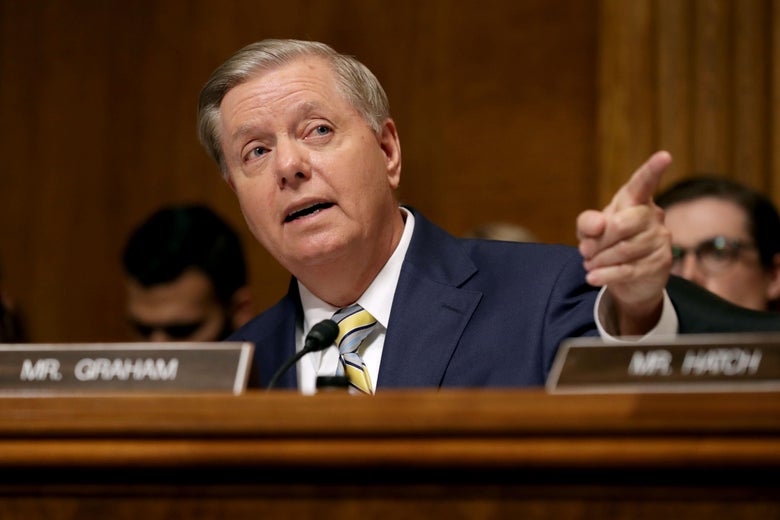 Sen Lindsey Graham points while speaking. A nameplate sits in front of him.