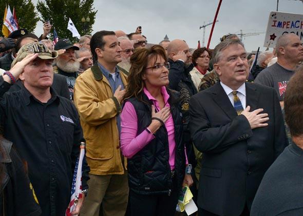 Former Vice Presidential candidate Sarah Palin, center, and Sen. Ted Cruz (R-TX), center left, hold their hands over their hearts during the national anthem as veterans, their families and supporters hold a rally at the WWII Memorial to protest its' closing on October, 13, 2013 in Washington, DC.