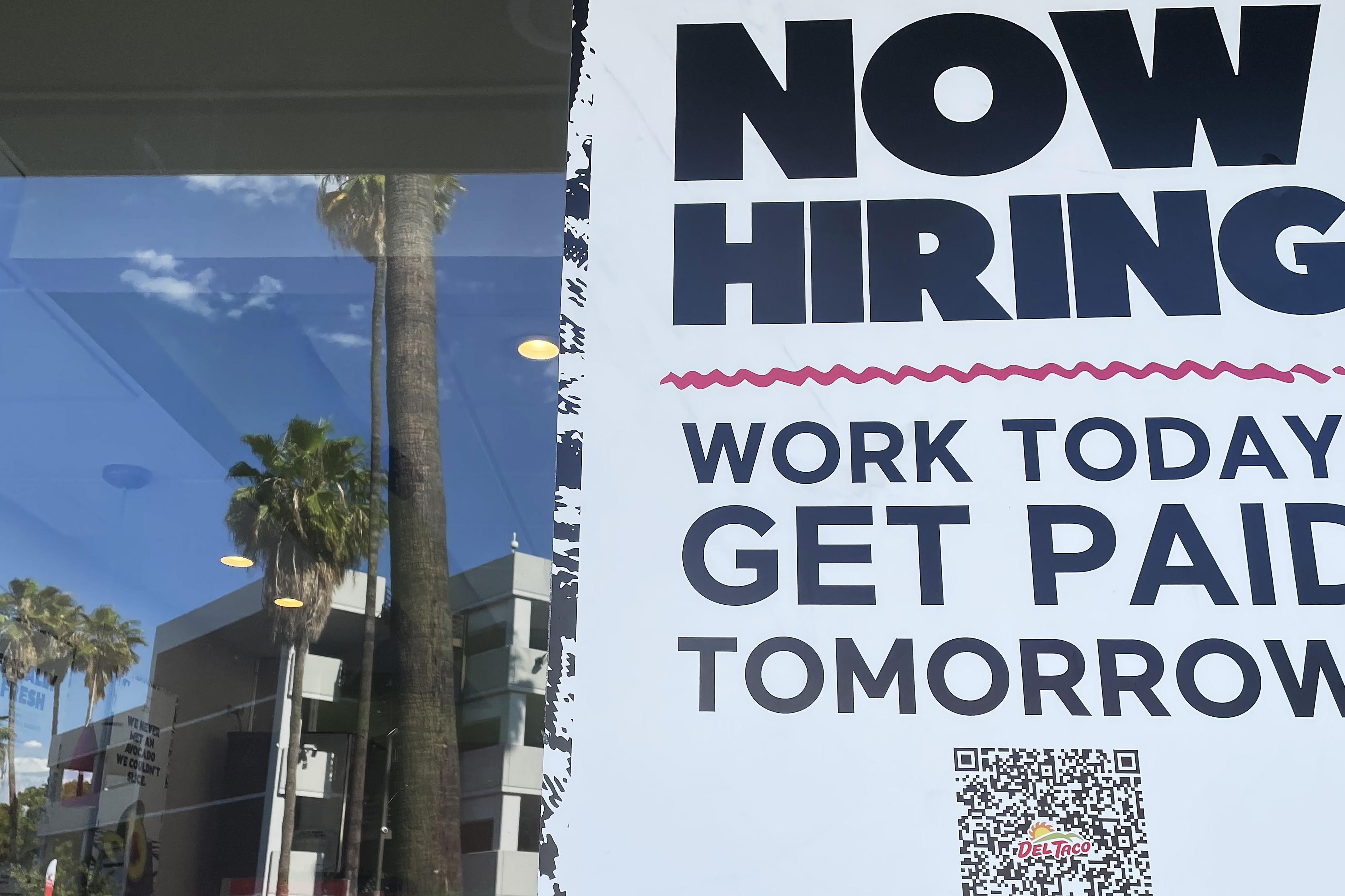 A sign that says "Now Hiring, Work Today, Get Paid Tomorrow" in the window of a Del Taco in Los Angeles