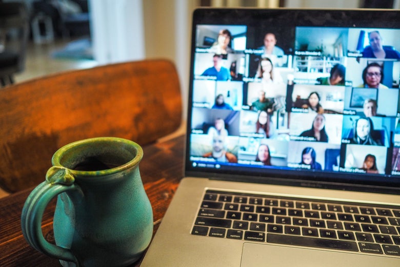 A mug sits next to a laptop displaying a Zoom filled with people.