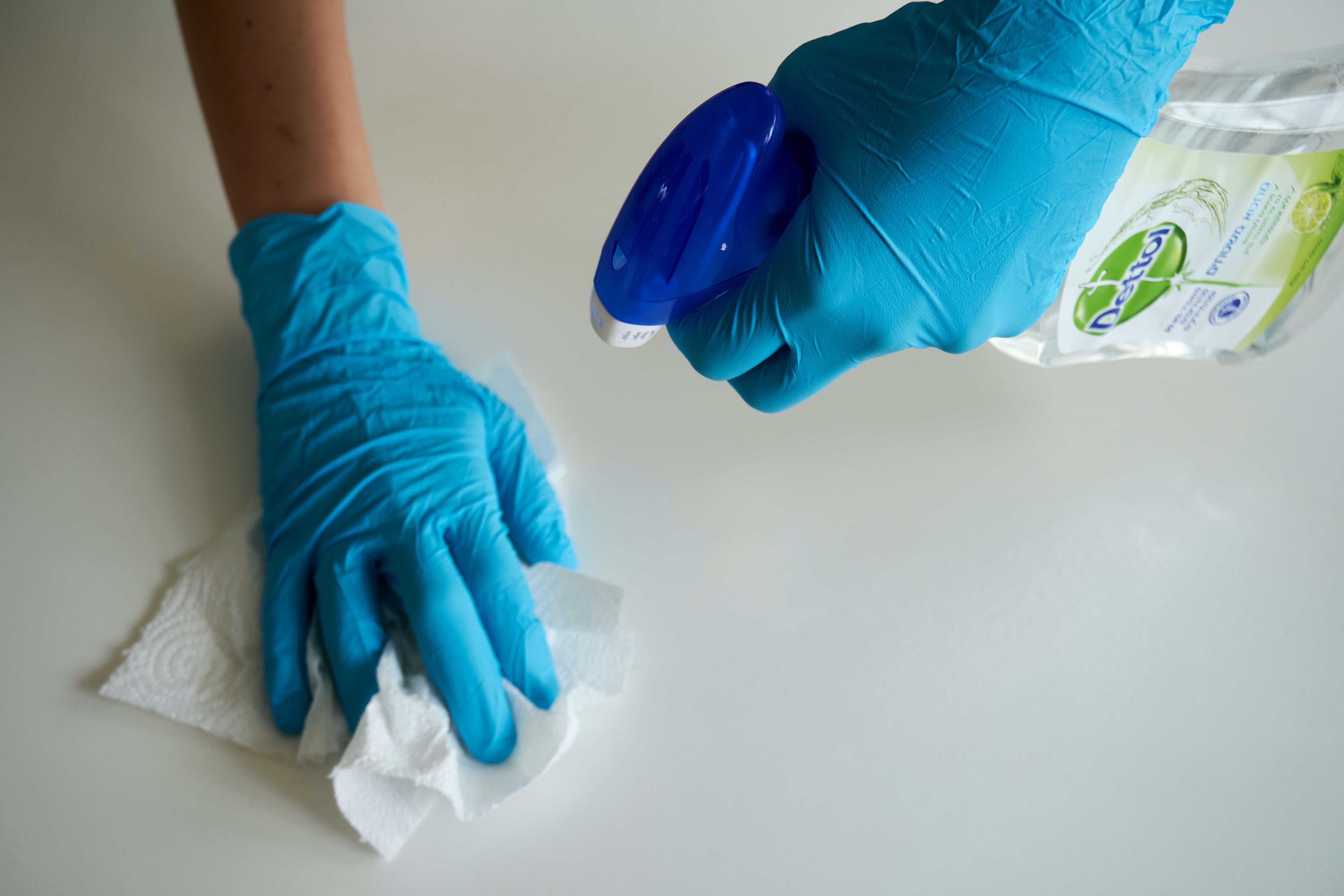 A person in gloves using disinfectant spray and a paper towel to clean a surface