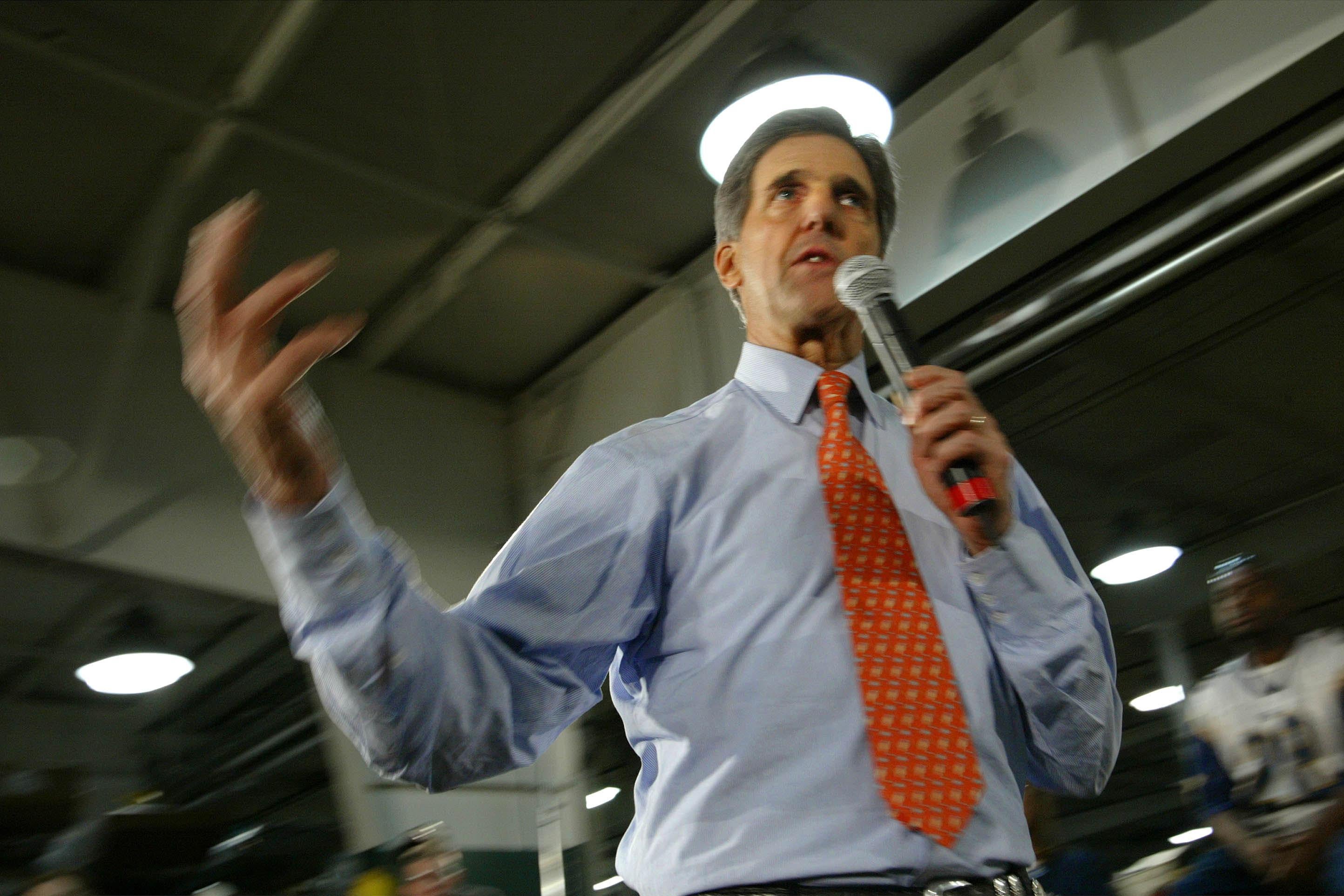 John Kerry, viewed from below, gestures while holding a microphone.