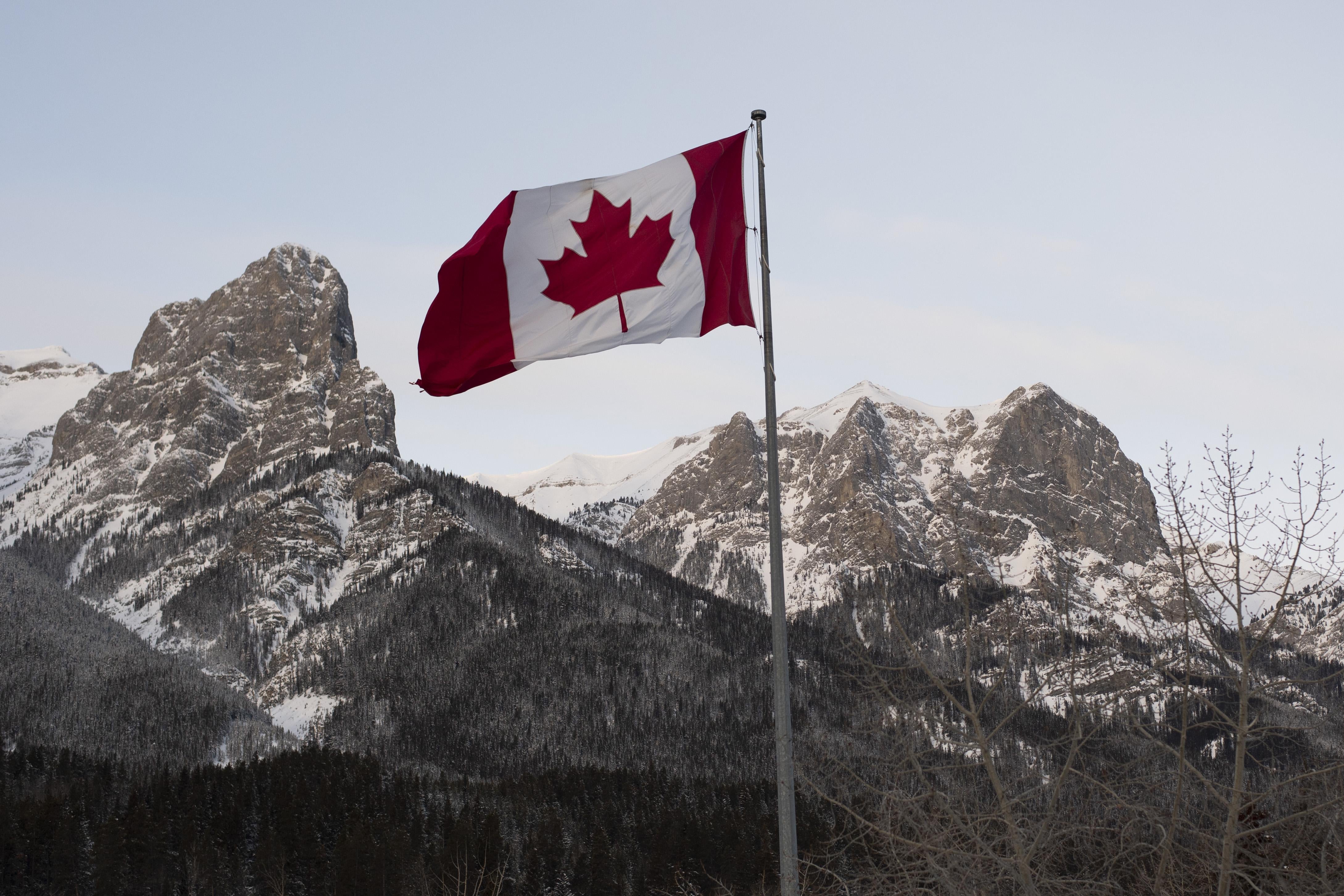 The Canadian flag flies over the Canadian Rockies.
