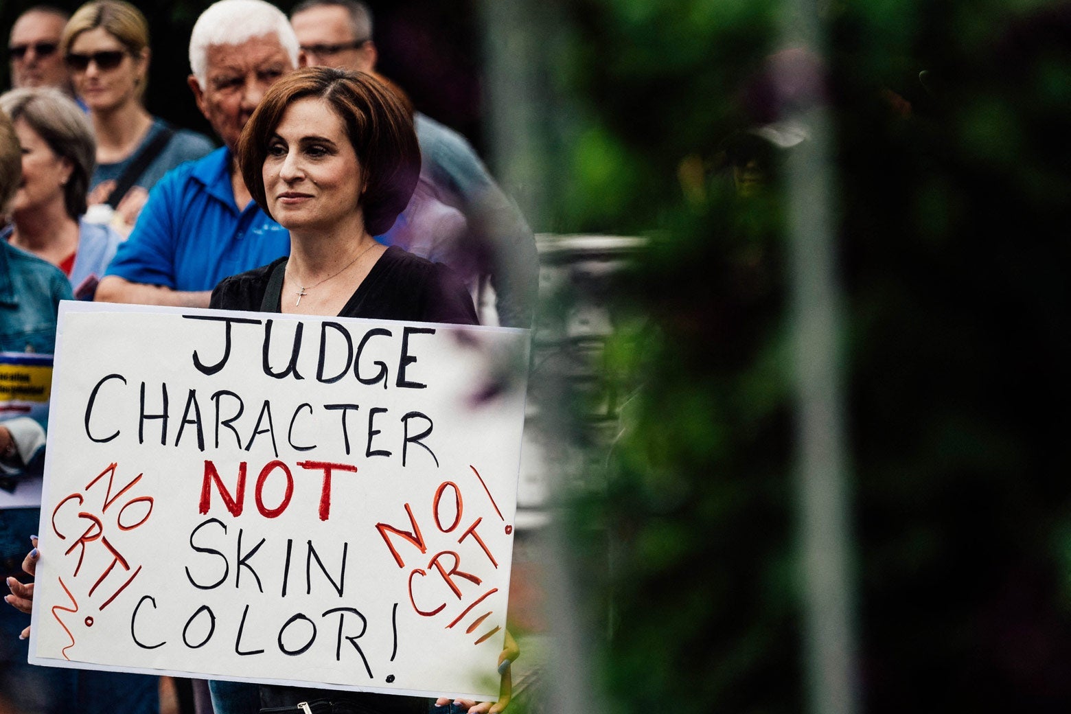 A woman holds a sign that says "Judge Character Not Skin Color! No CRT!" as she stands among other protesters