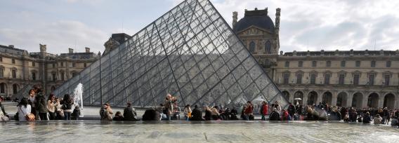 People enjoy the sunny spring weather near the Louvre Pyramid at the Cour Carree of the Louvre Museum on April 7, 2013, in Paris.