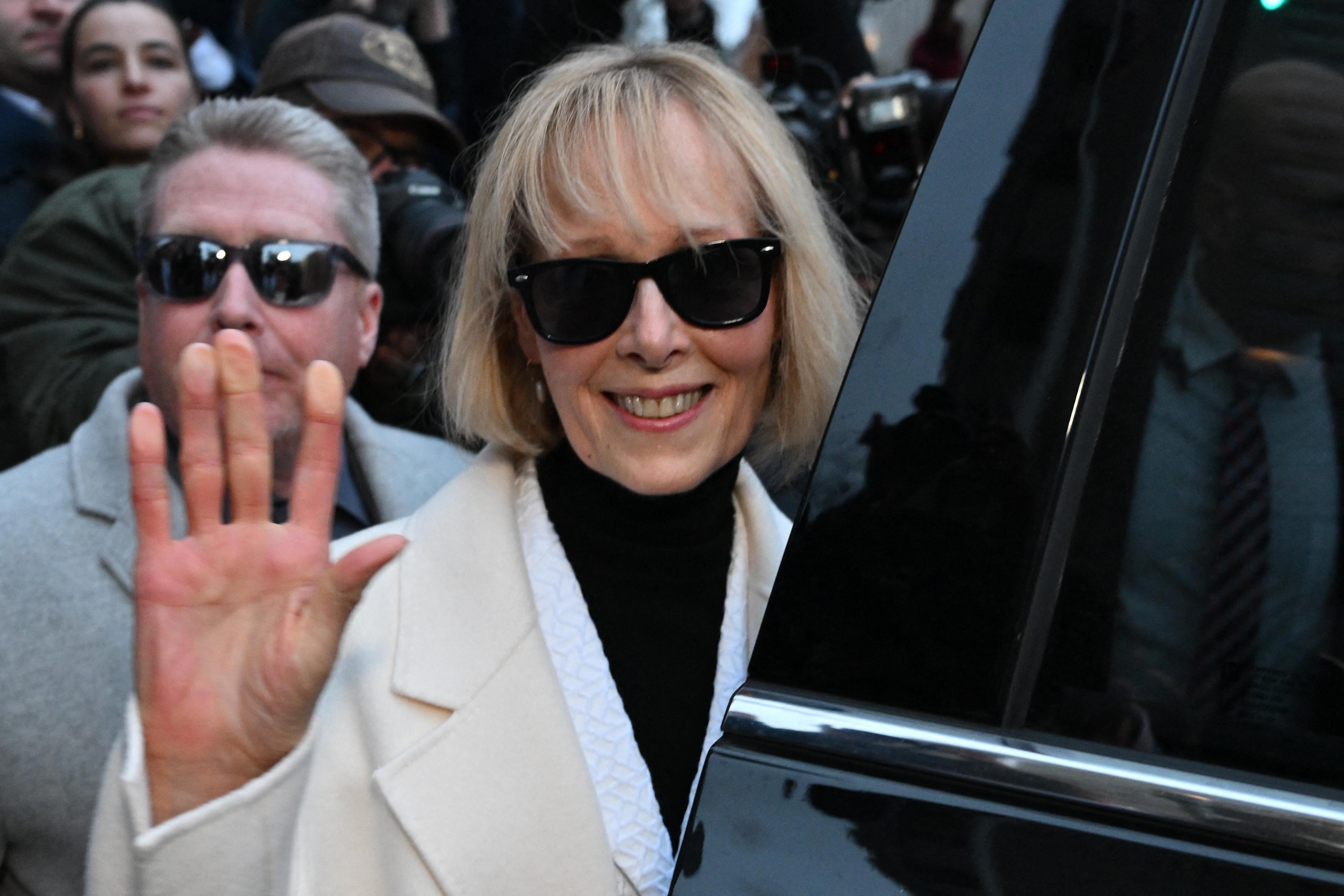 Writer E. Jean Carroll waves as she leaves federal court, as she enters her SUV. She is smiling and wearing sunglasses.