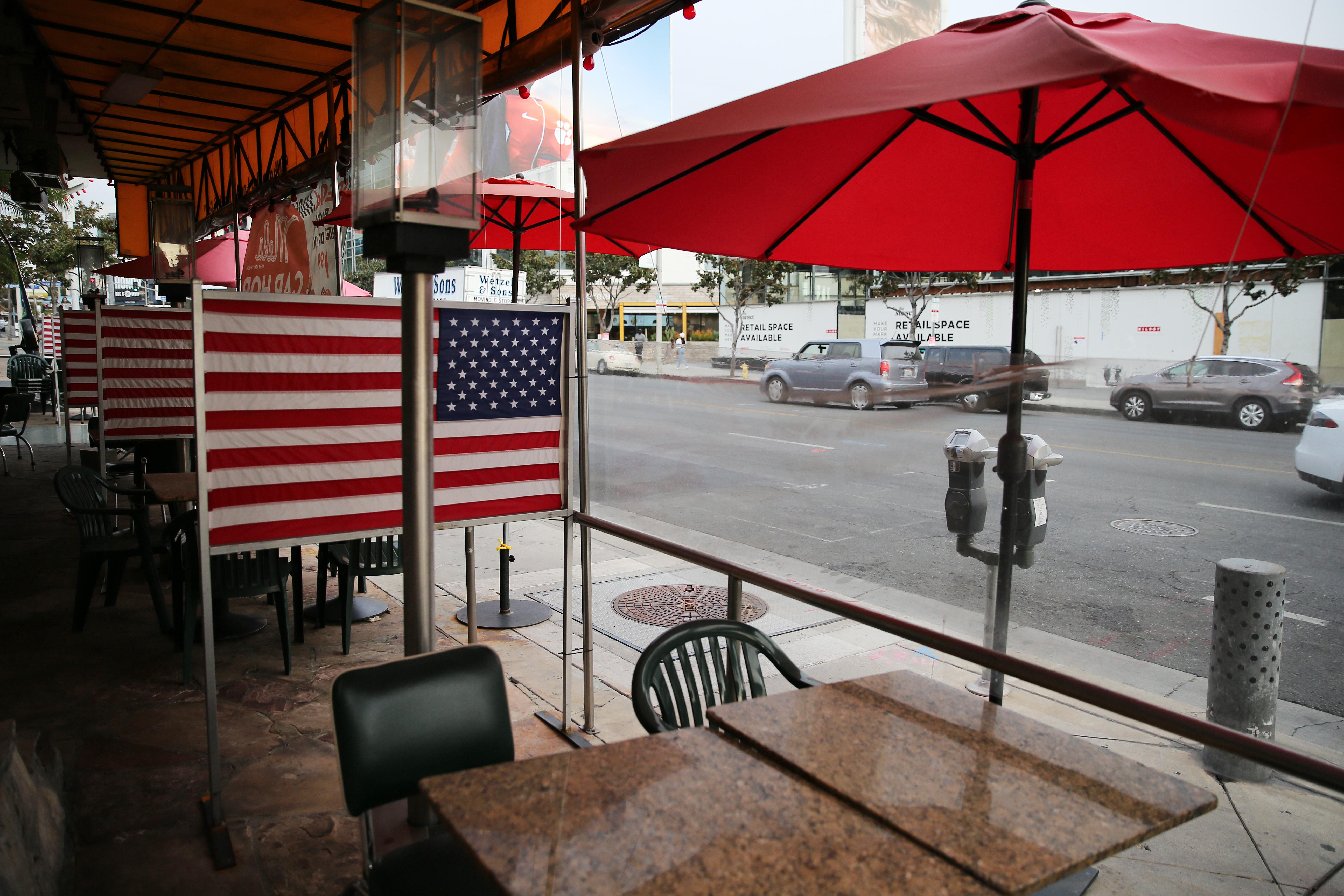 Empty outdoor dining tables with umbrellas and American flag dividers between them