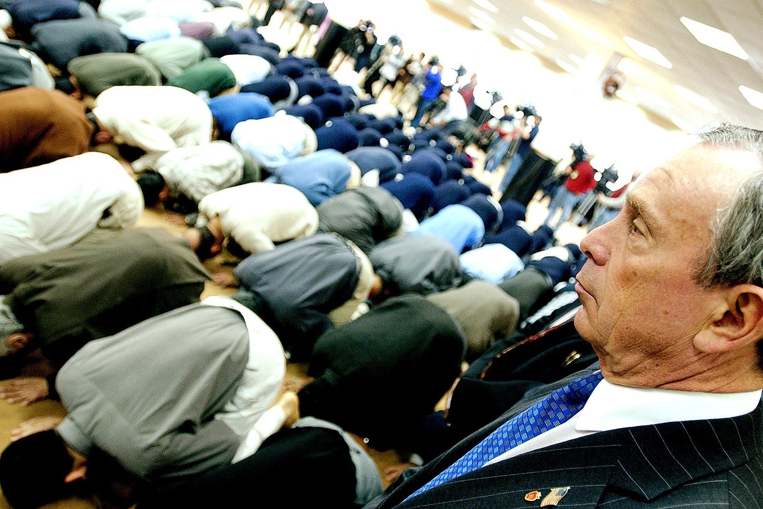 Michael Bloomberg looks over Muslims kneeling in prayer.