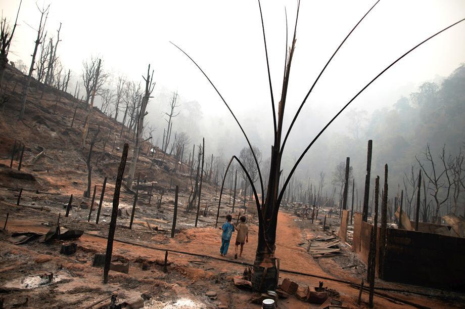 Two boys walk through the ruins of the Ban Mae Surin refugee camp near Mae Hong Son, Thailand, on March 24, 2013. At least 42 people have died in a fire at a camp that is home to thousands of refugees from Burma.