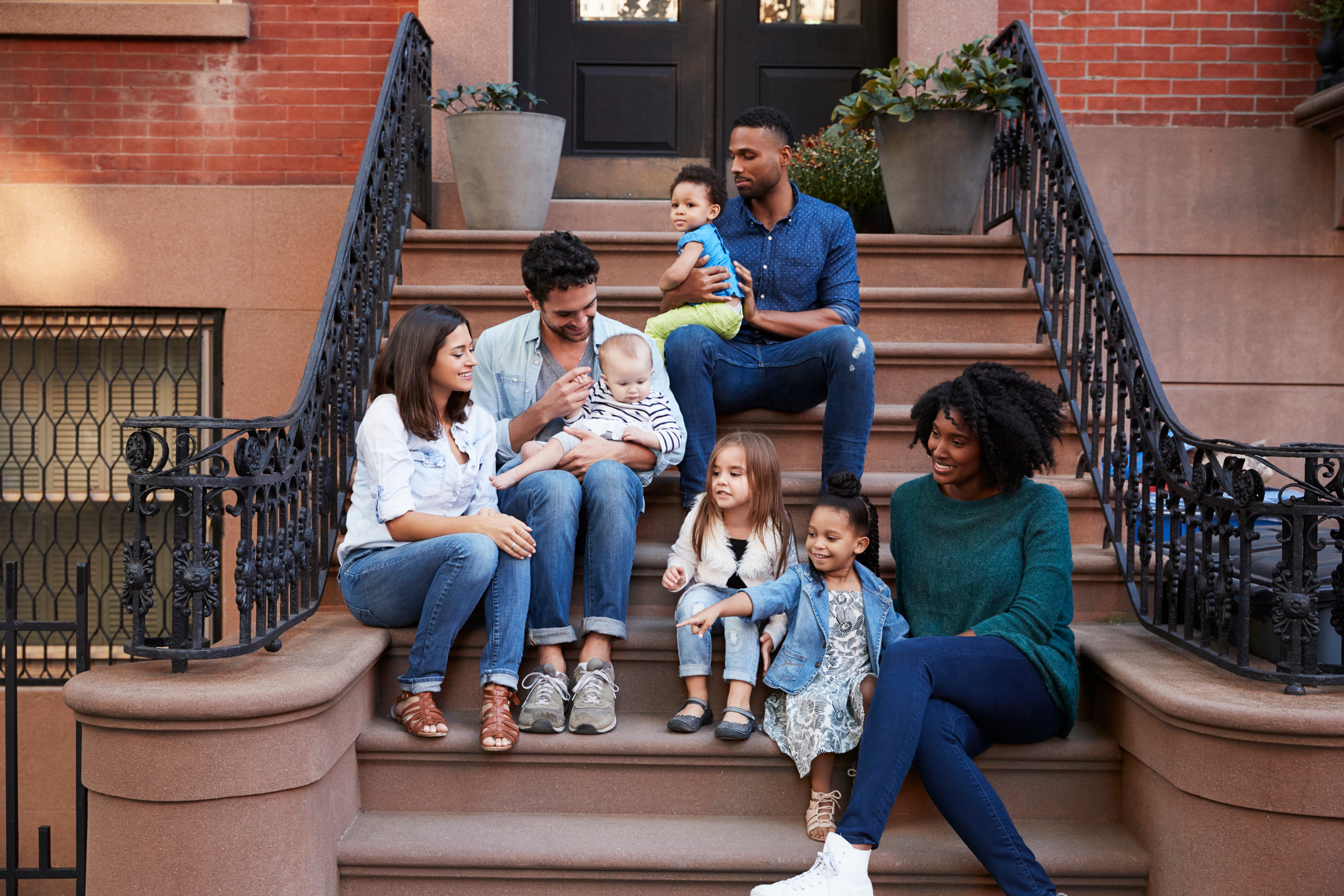 Four parents and four kids are sitting chatting on a stoop.