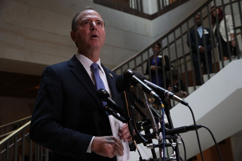 Schiff speaks into a microphone in front of a stairway in an open area of a building with marble walls.