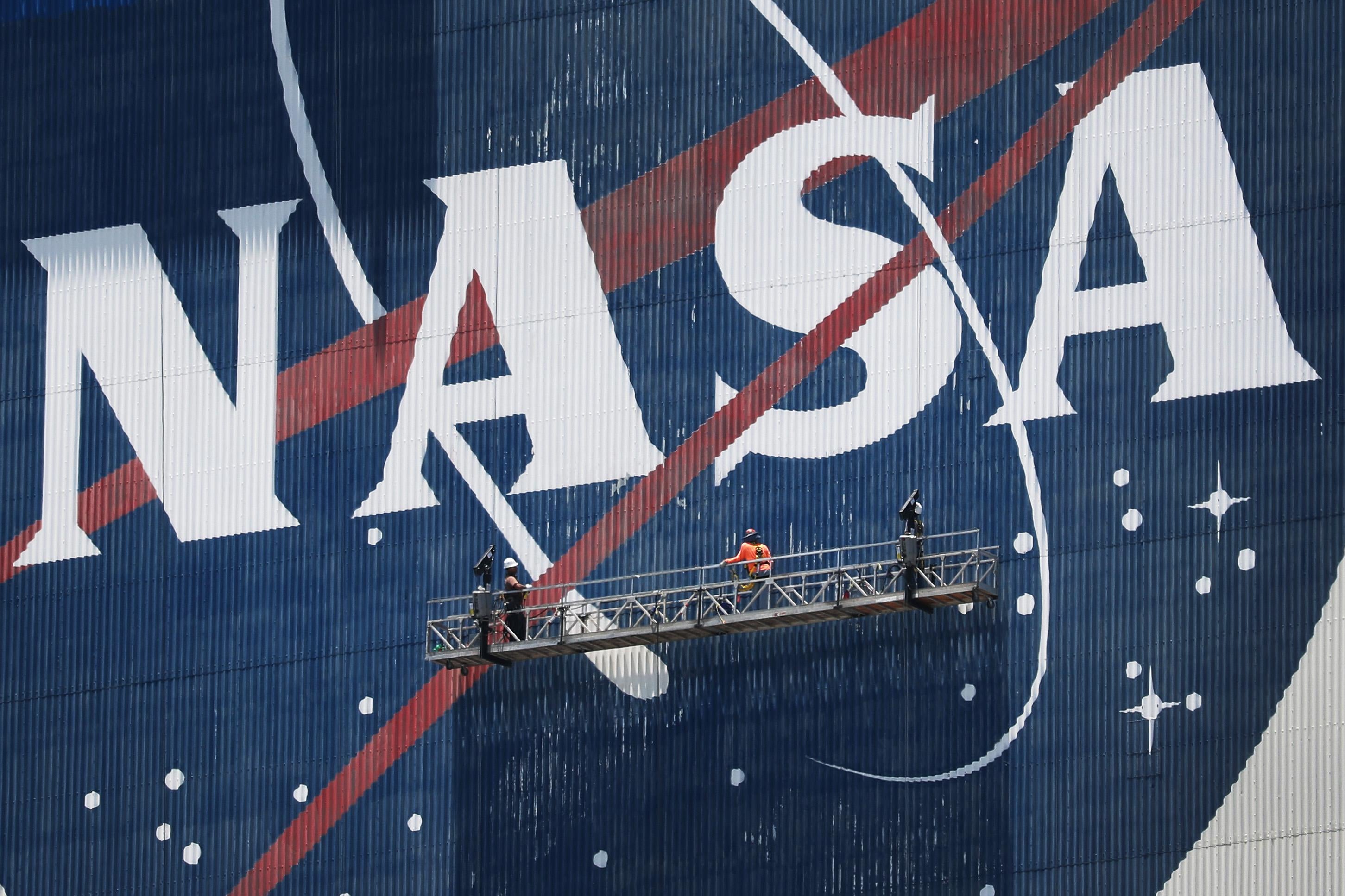 Two people on a scaffolding in front of a giant NASA logo