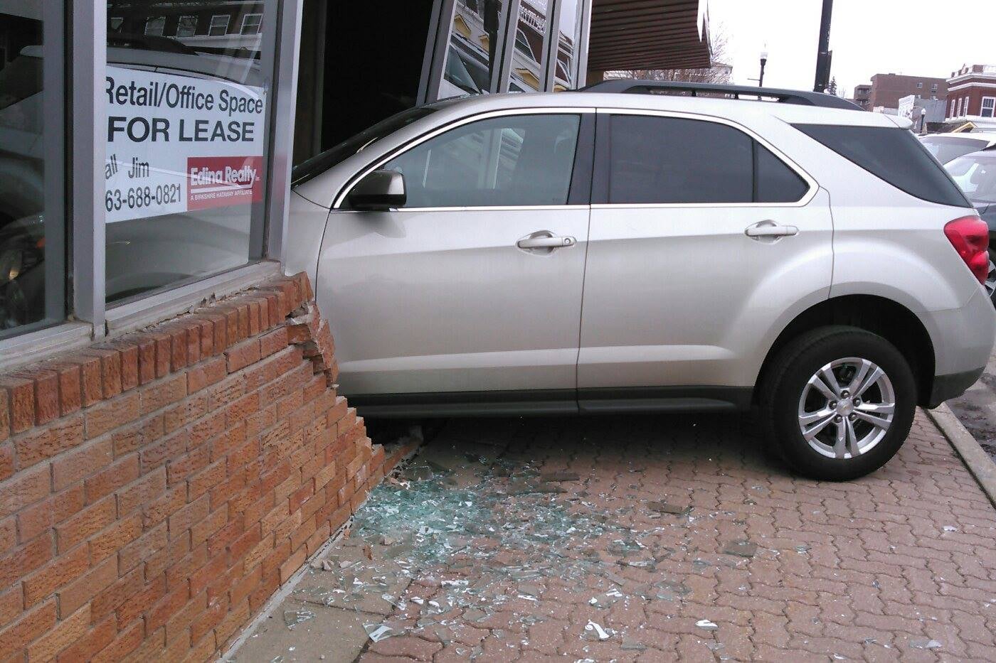 A car surrounded by shattered glass that has crashed through the front of a building.