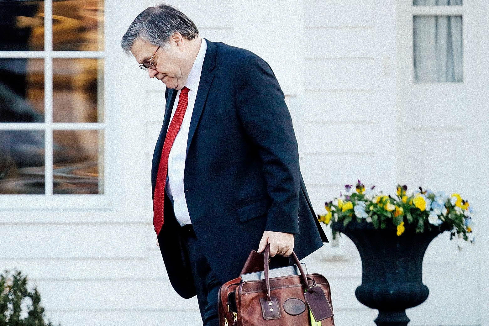 Bill Barr carries a briefcase and looks down