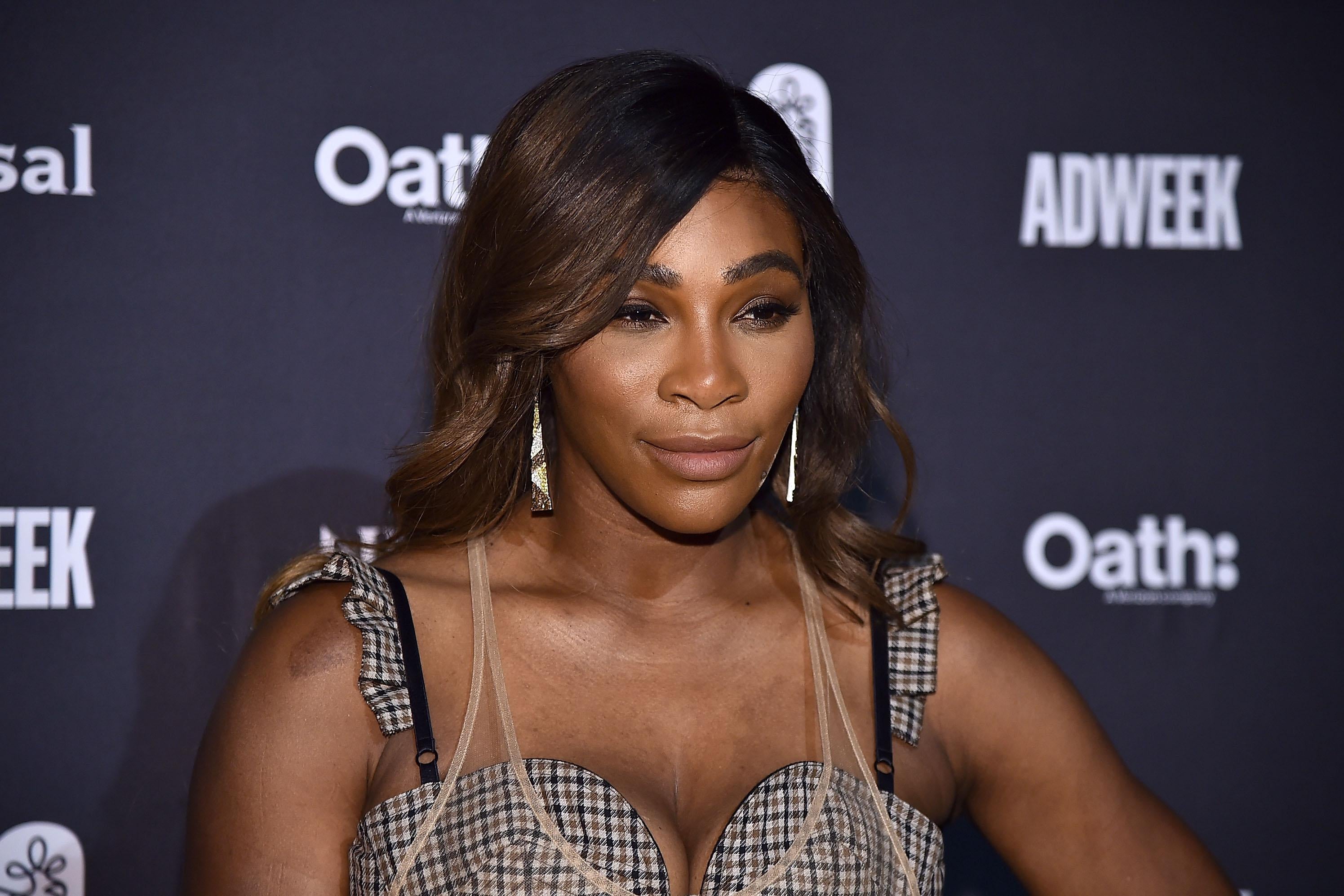 Serena Williams stands against a black backdrop, wearing a plaid sleeveless dress.
