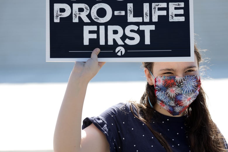 A woman wearing a face mask holds up a sign that says "Pro-Life First."
