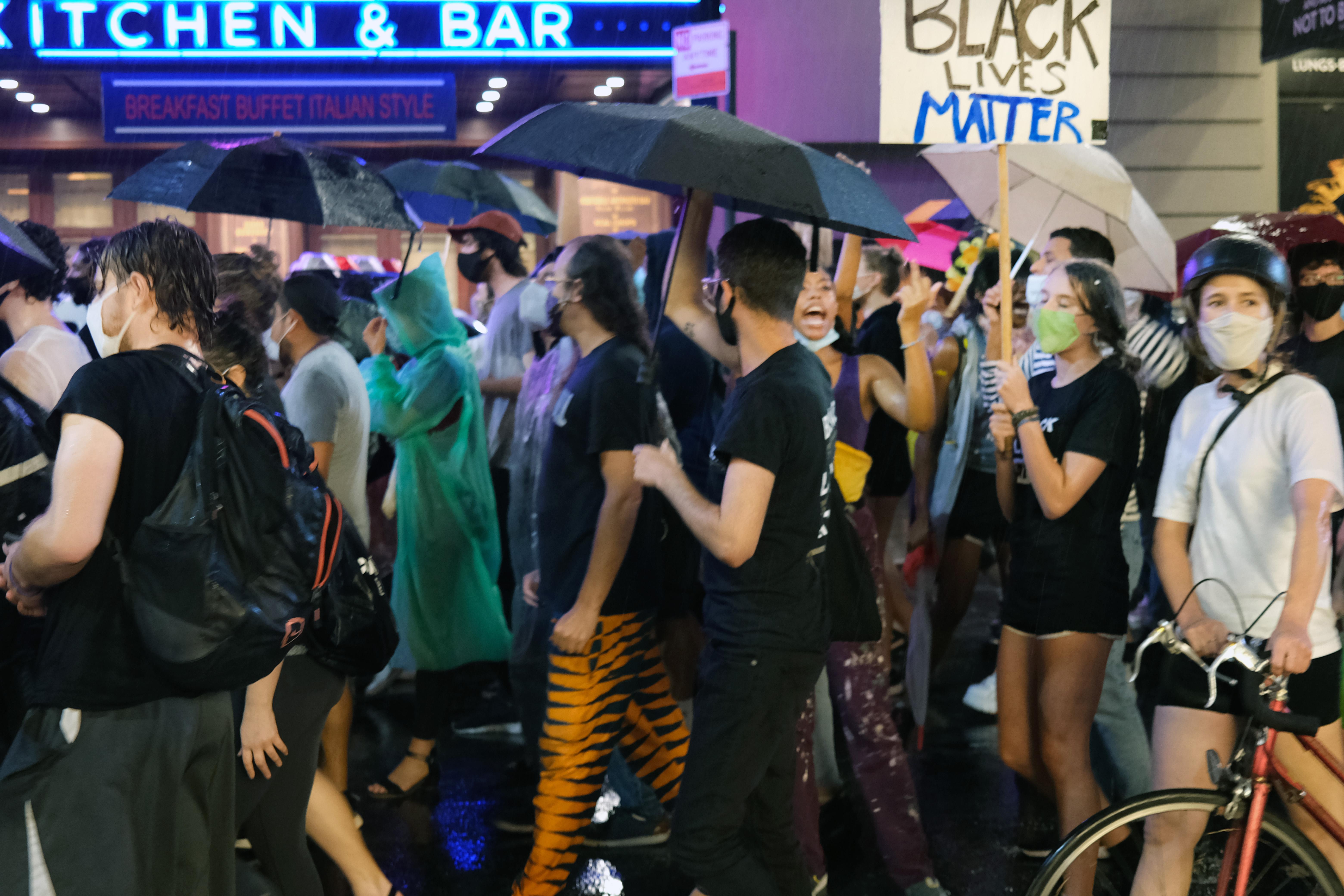 People carrying umbrellas and signs march in the rain in a protest.