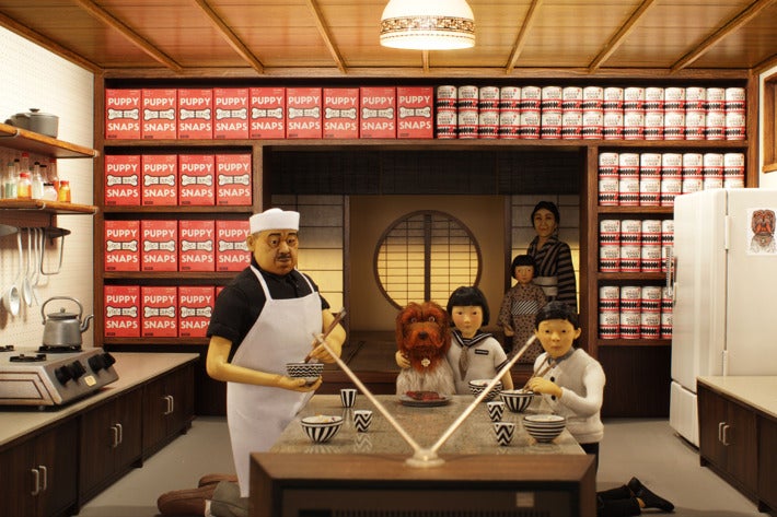 A Japanese family (complete with dog) sits at a dining room table and watches TV in Wes Anderson's Isle of Dogs.