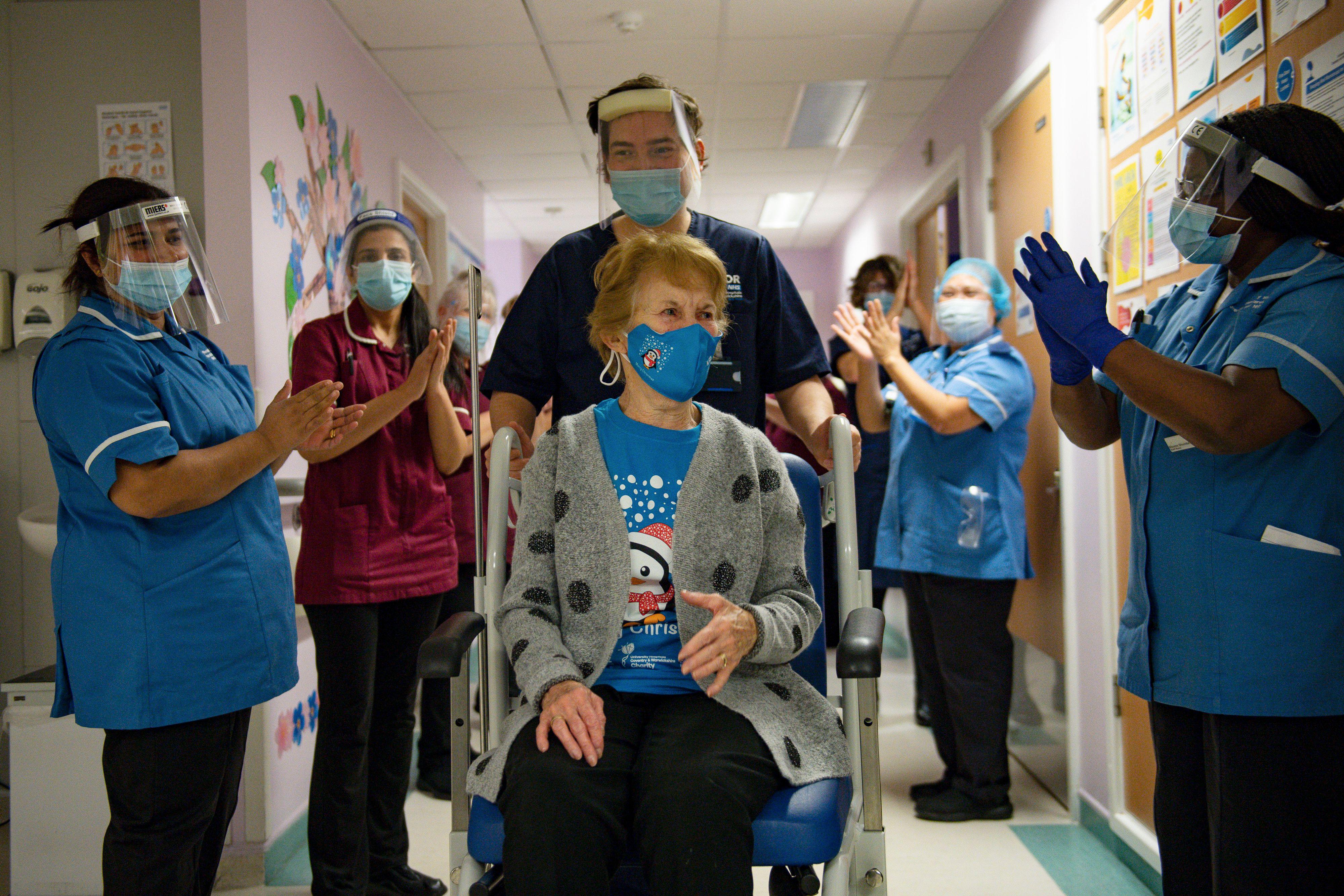 A woman in a wheelchair surrounded by medical professionals clapping