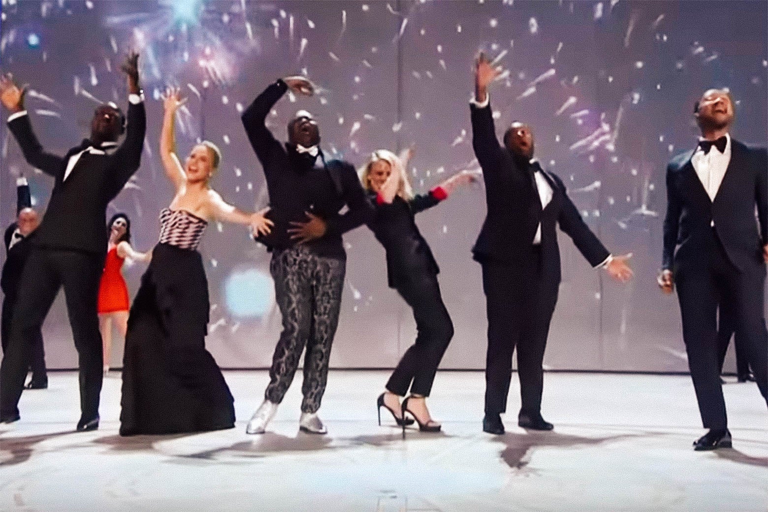 Fireworks go off on a projection screen behind a bunch of dancing TV stars.