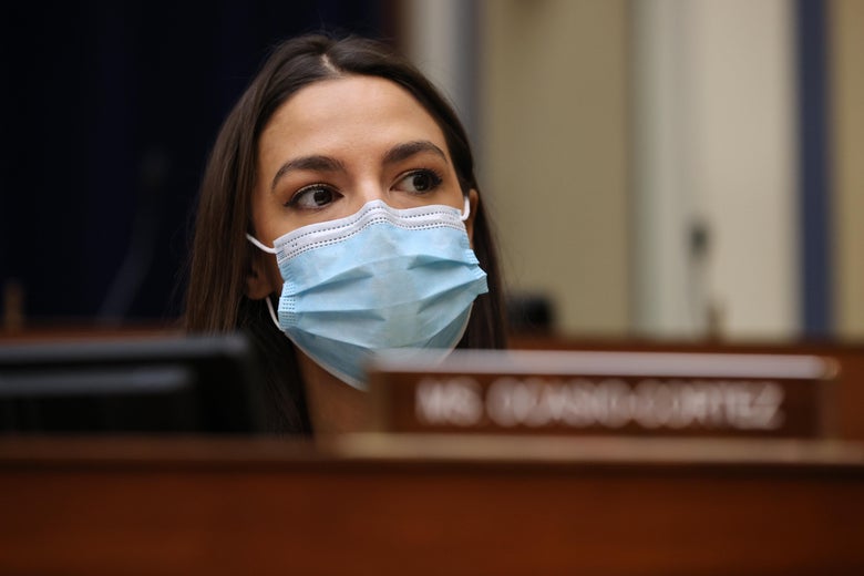 A woman with dark hair and a face mask sits in a hearing room.