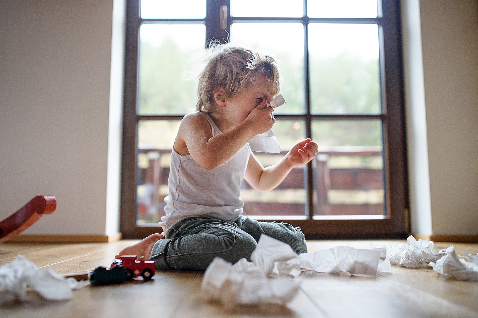 A young blond-haired boy surrounded by tissues sneezing into one.