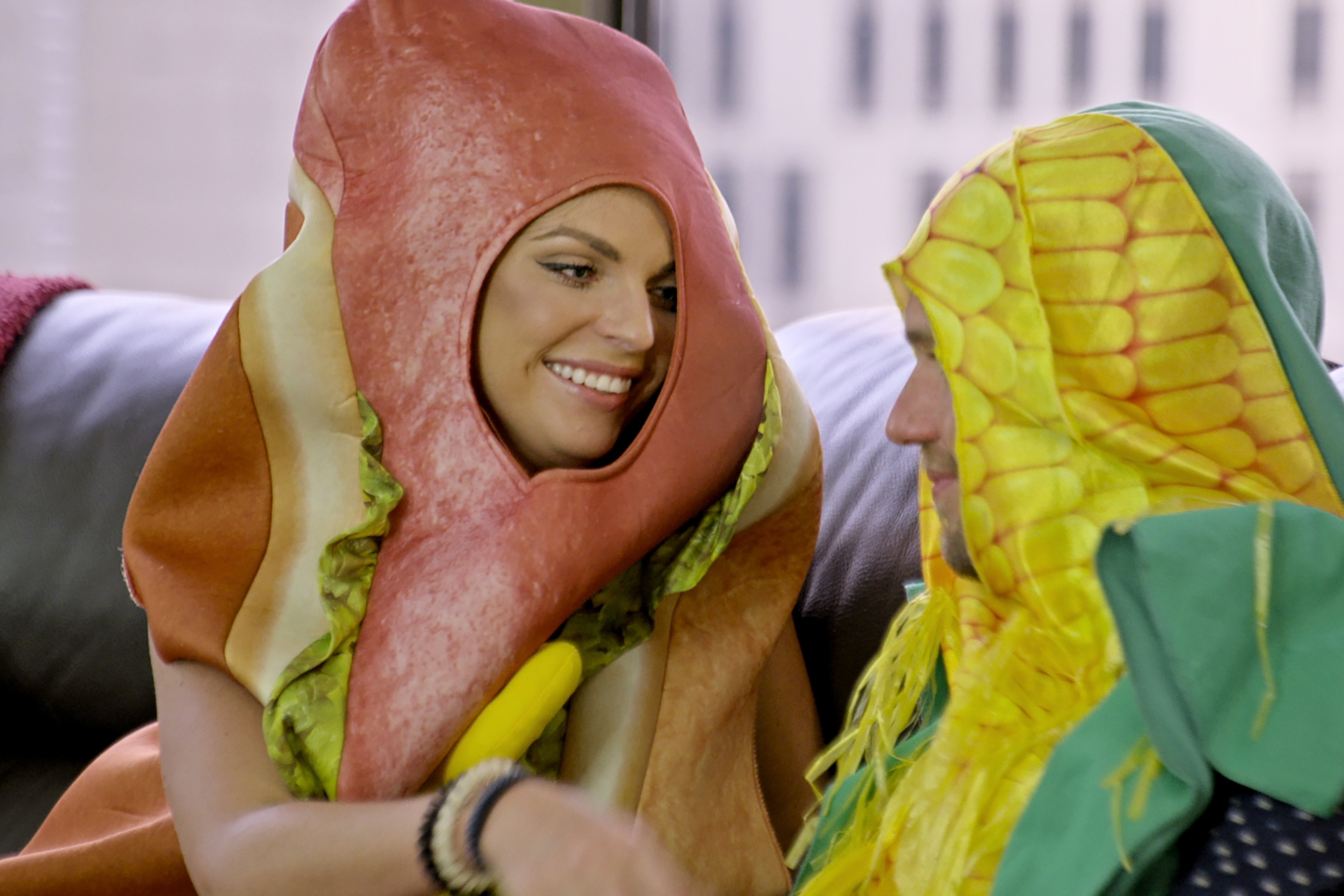 A woman wearing a hot dog costume and a man wearing an ear of corn costume.