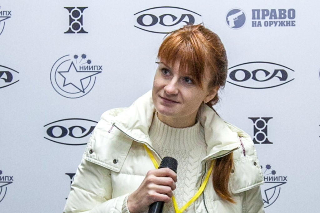 Butina, seated, holds a microphone at a press conference.