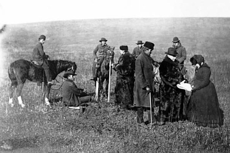 Alice Fletcher holding the bottom of a document that allots a portion of land to Nez Perces as others stand by.