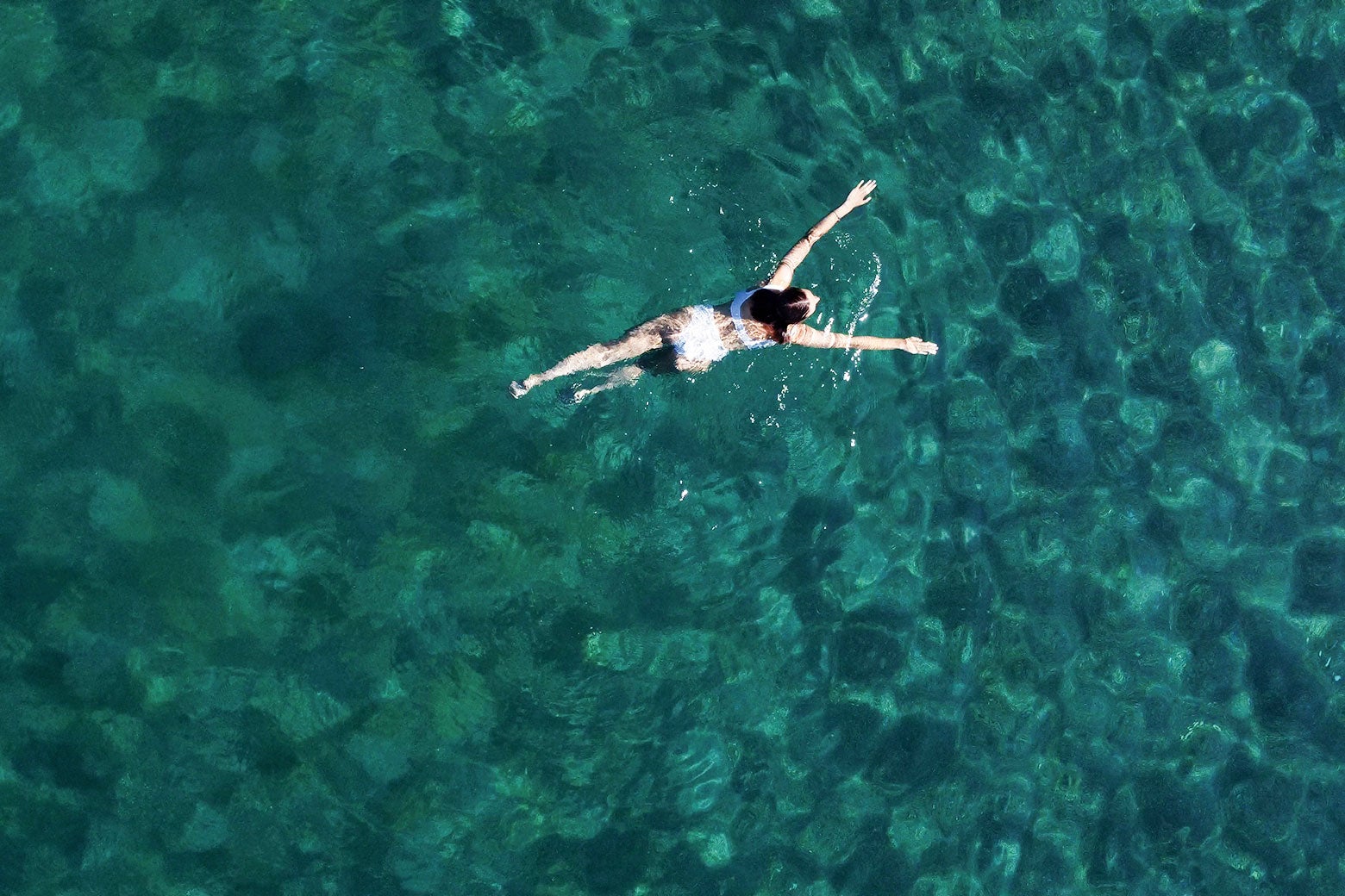 A woman is seen from above swimming in appealing bluish-green water. 